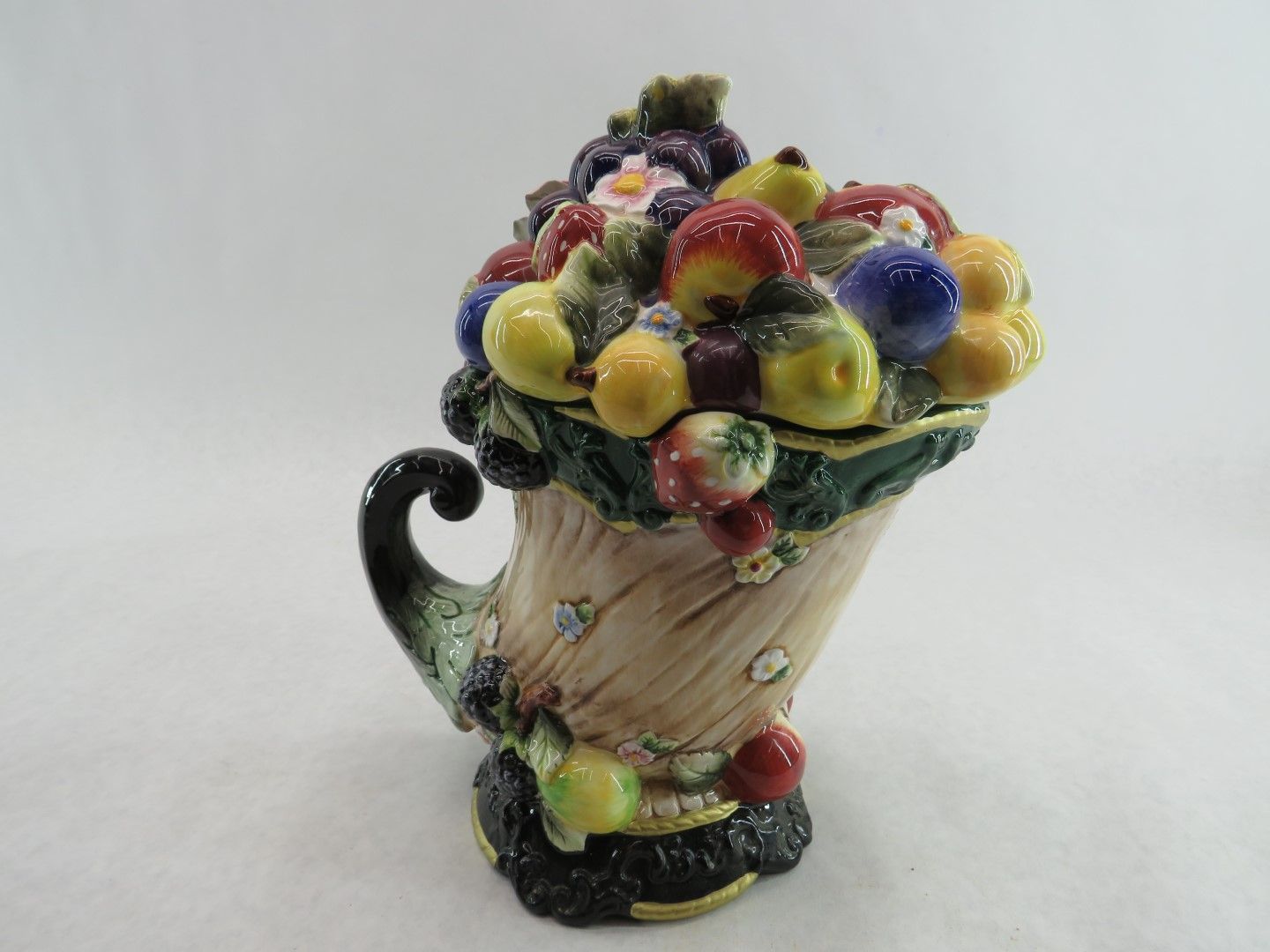 Ceramic cornucopia-shaped container overflowing with colorful, sculpted fruit.