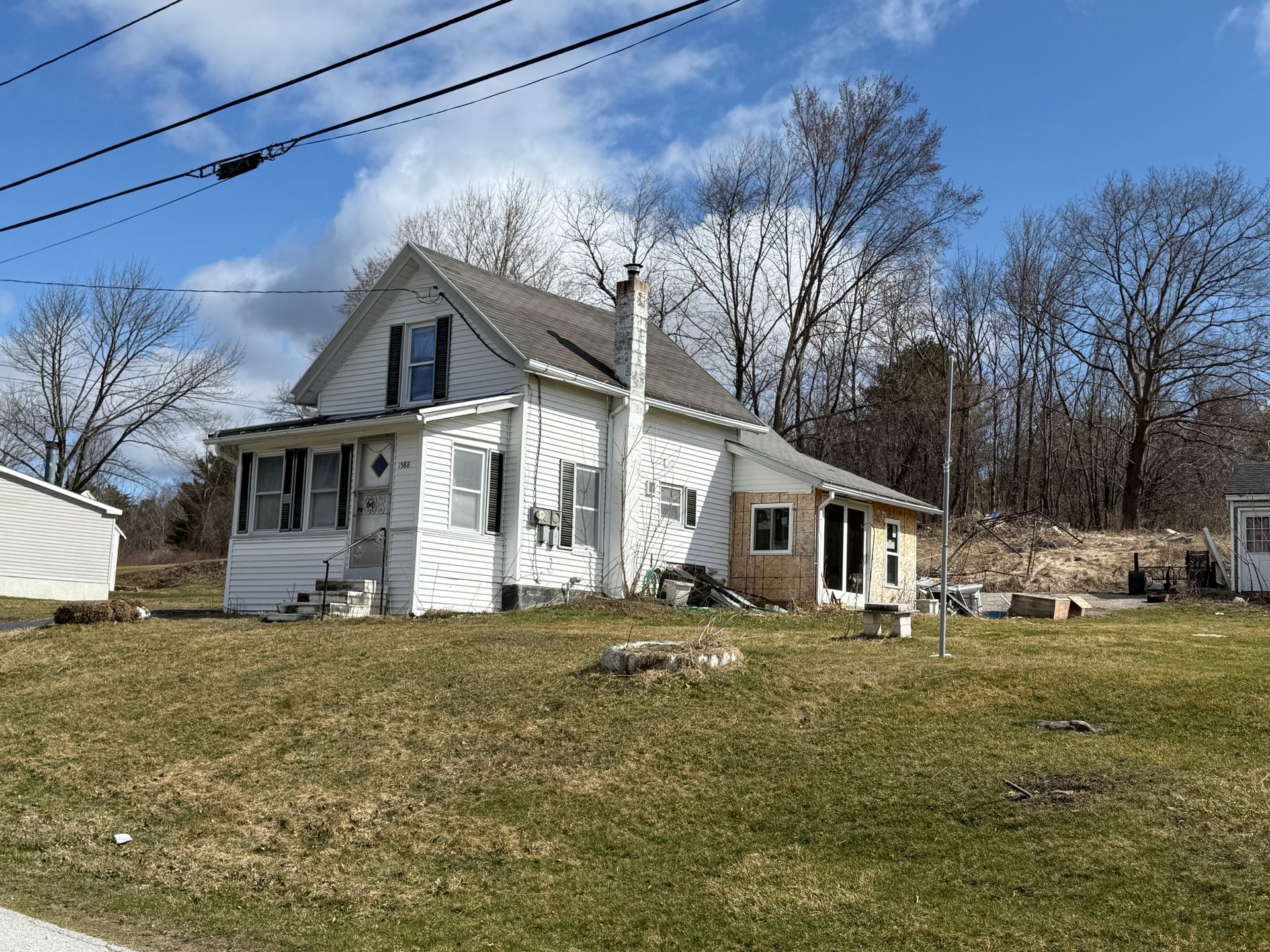 White house with chimney, flanked by bare trees and power lines, against a blue sky.