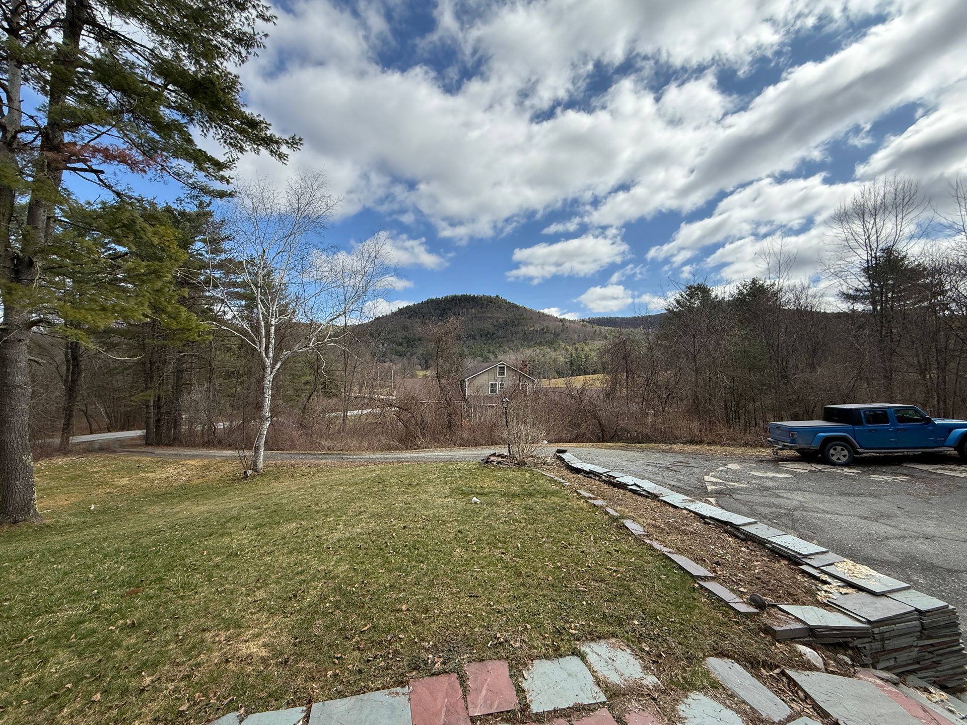 Lawn with a mountain backdrop, a blue truck, trees, and a cloudy sky.