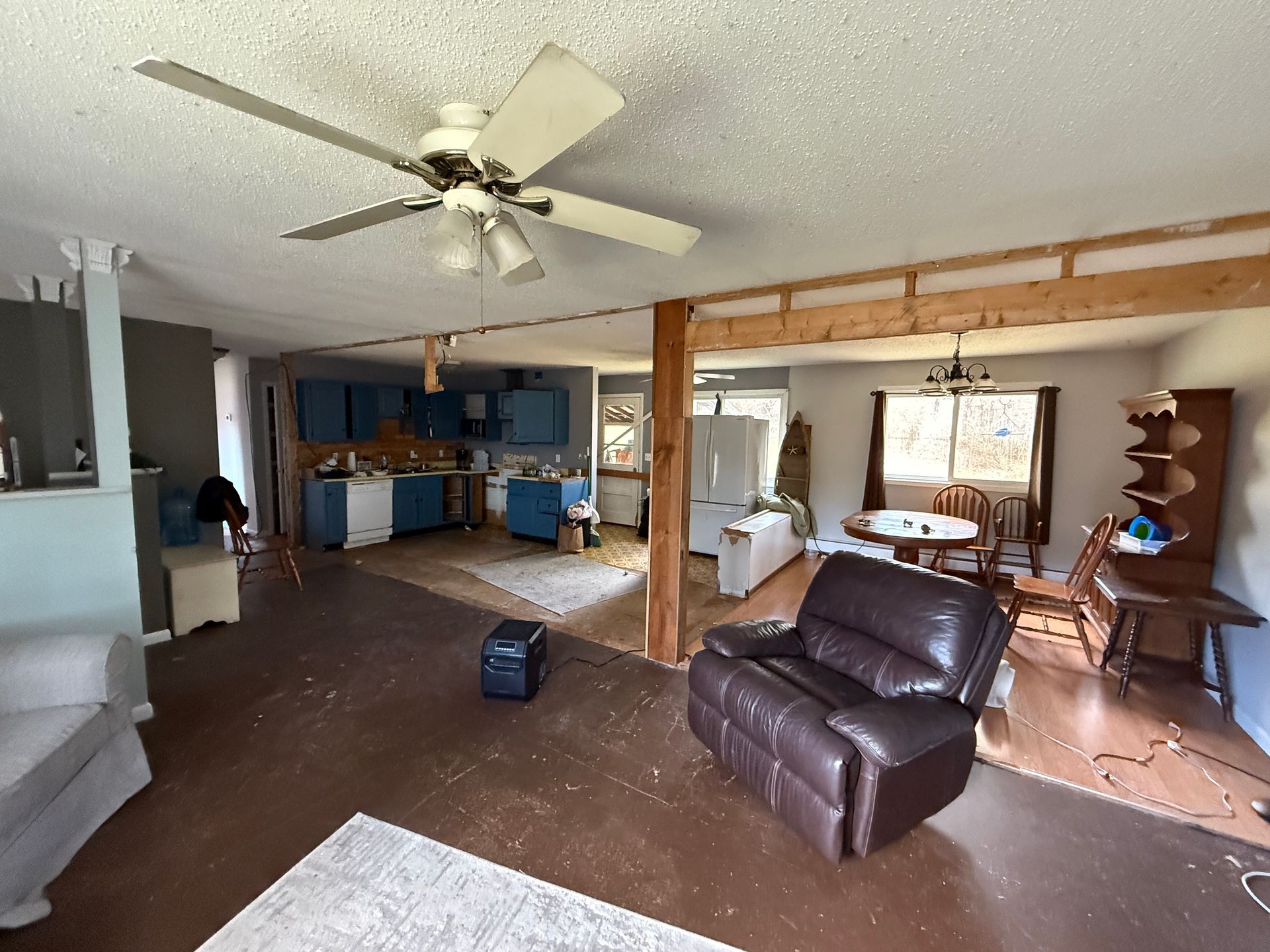 Open-concept living space with partial kitchen visible. Brown flooring, blue cabinets, and a brown recliner are present.