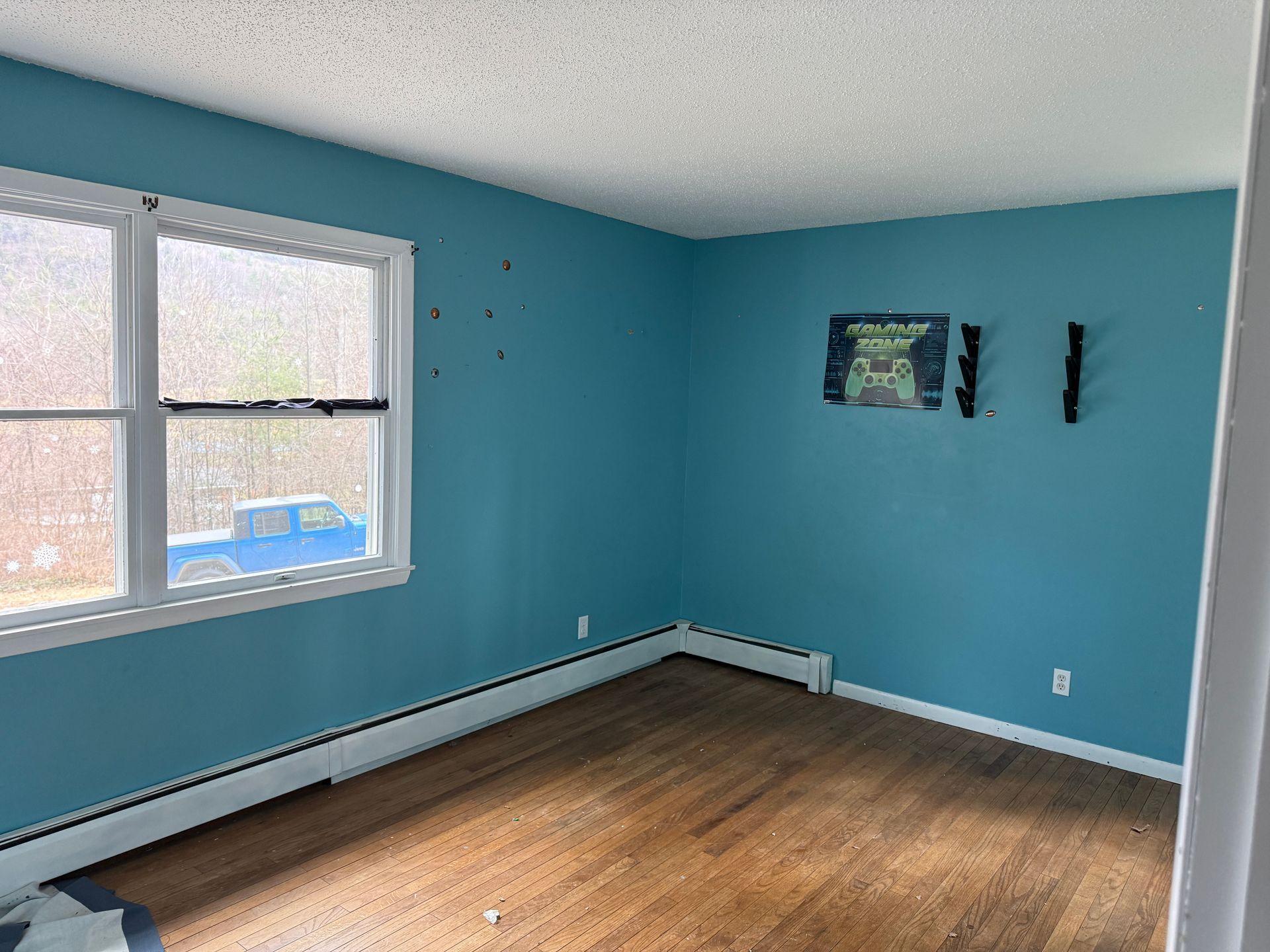 Empty room with blue walls, hardwood floor, white trim, and a window.