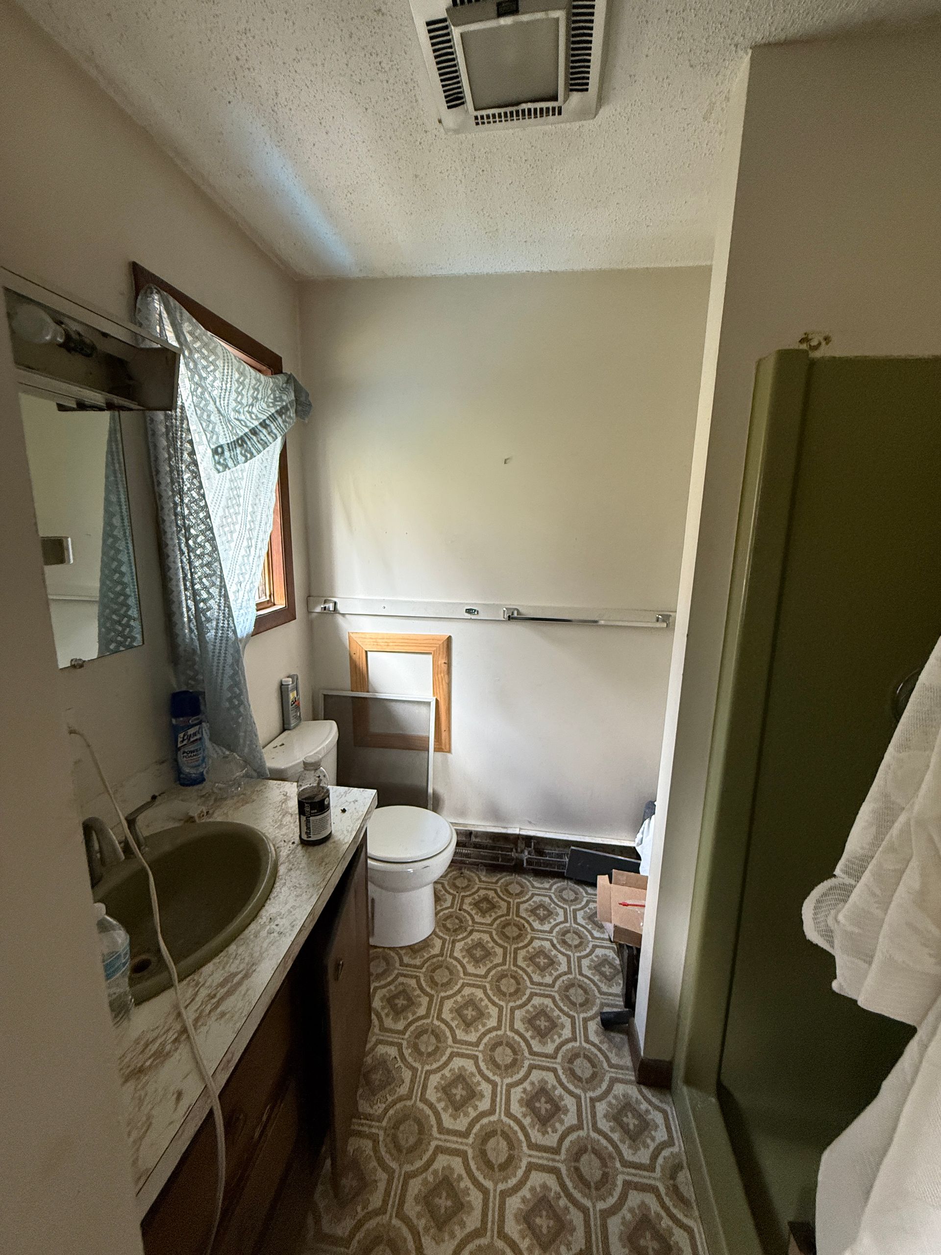 Bathroom with sink, toilet, shower, and patterned floor. Beige walls, olive green shower door, and window.