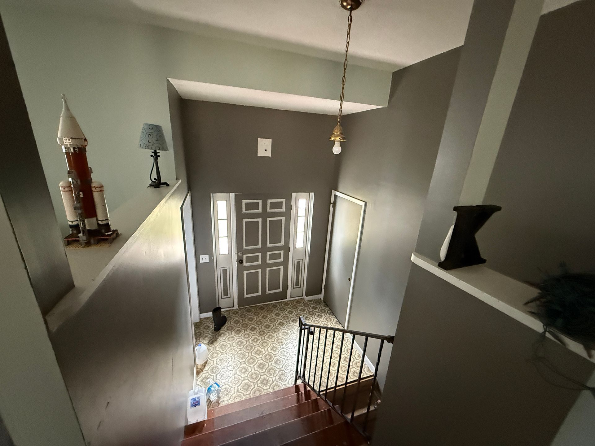 Entryway with a gray door, staircase, and shelves with decorations.