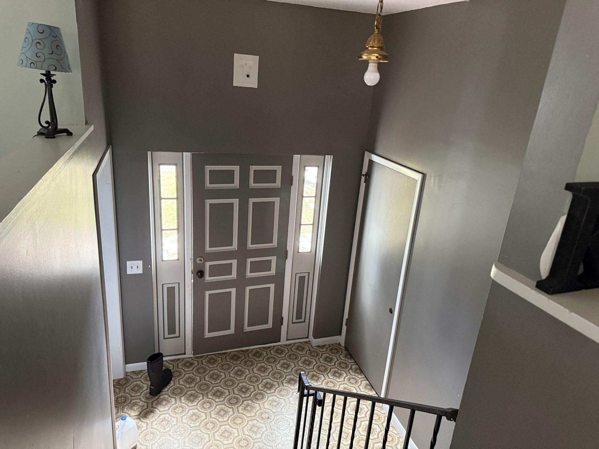 Entryway with gray walls, front door, patterned floor, and a hanging light fixture.