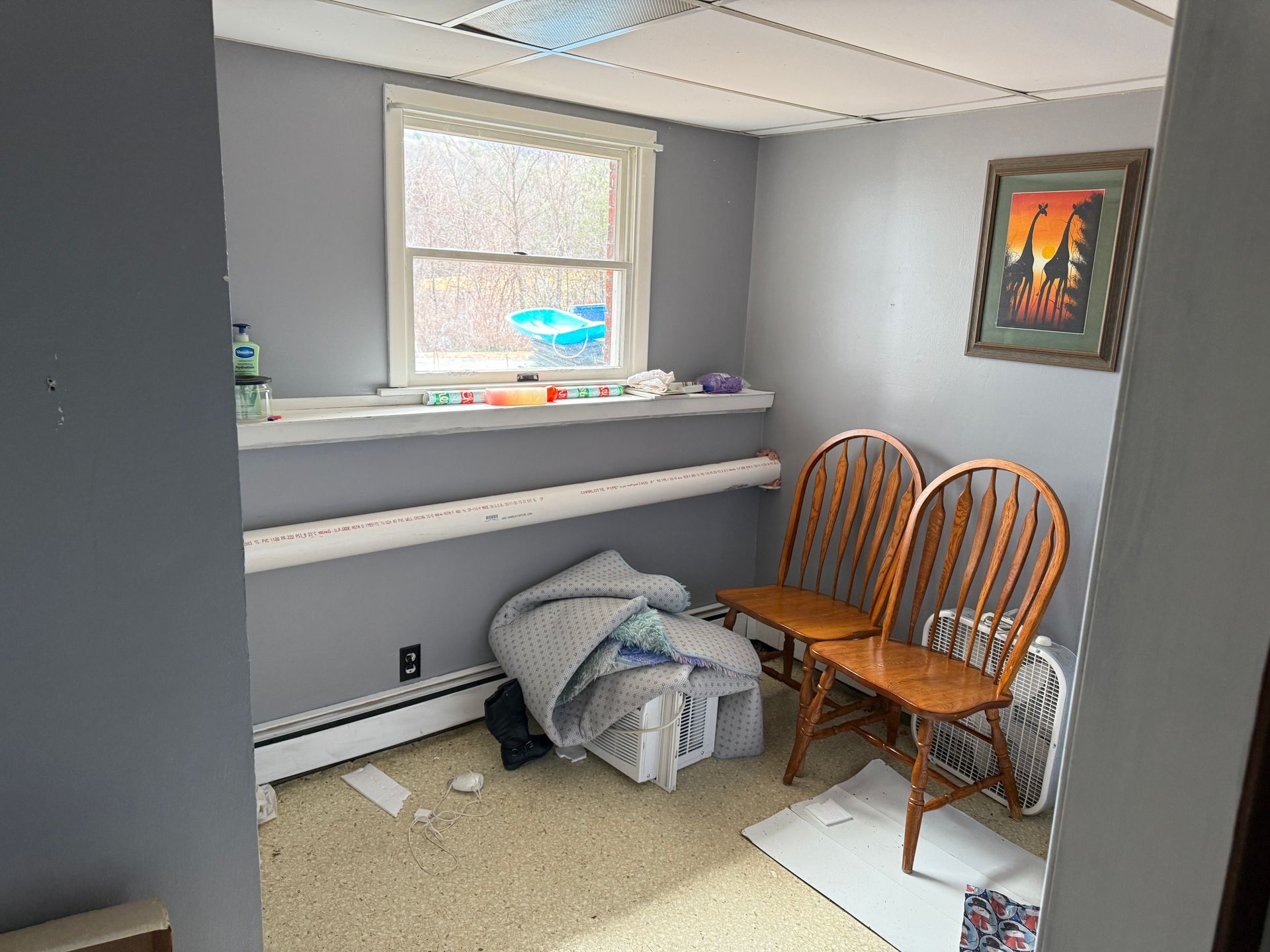 Small room with gray walls, window, two wooden chairs.