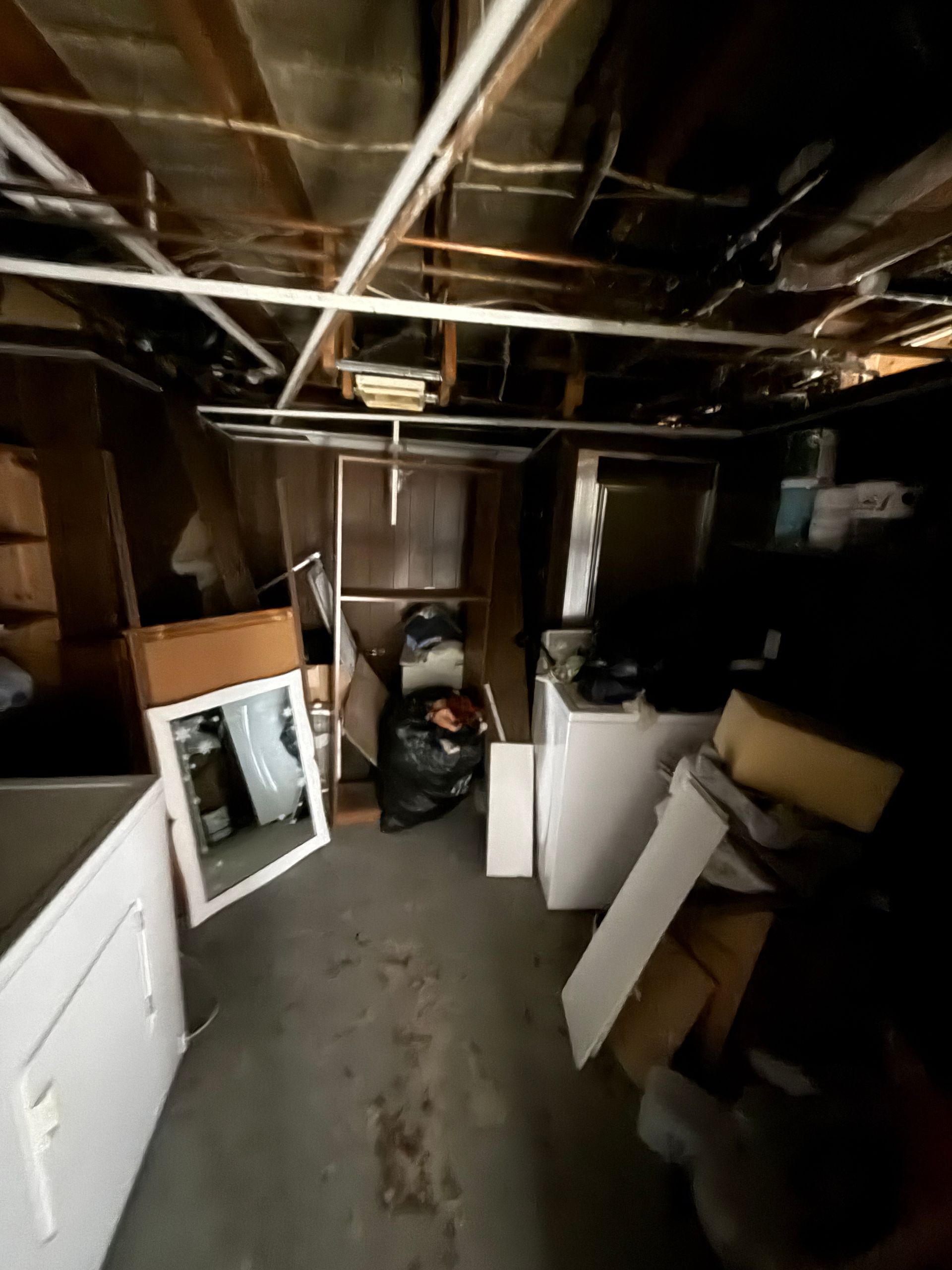 Storage room with exposed ceiling beams, various items including cabinets, mirror.