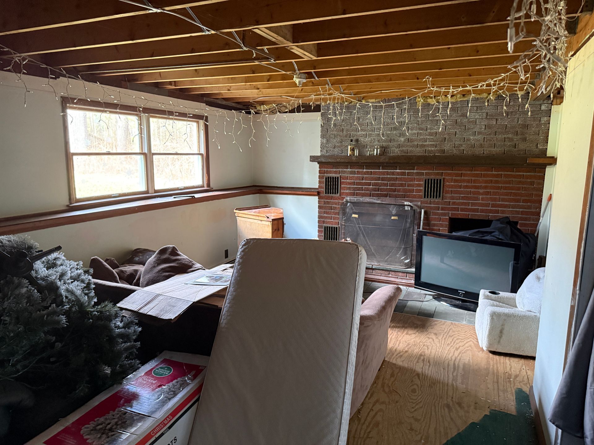 Interior of a room with exposed ceiling beams, fireplace, window, and various furniture items.
