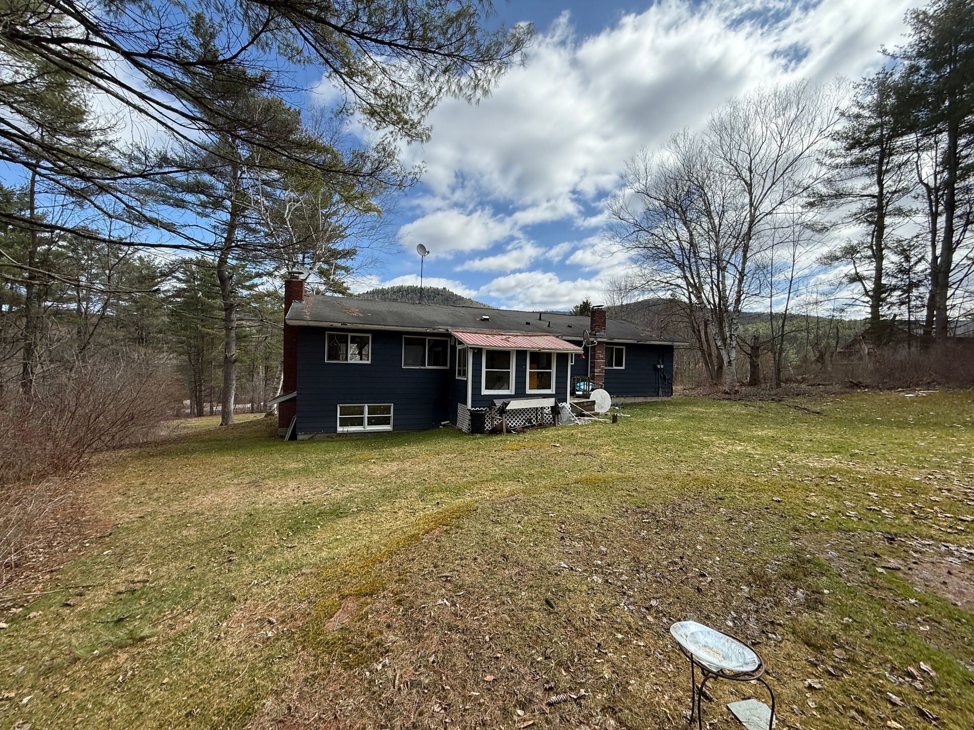 Dark blue house with red roof, set in a grassy yard, surrounded by trees under a cloudy sky.