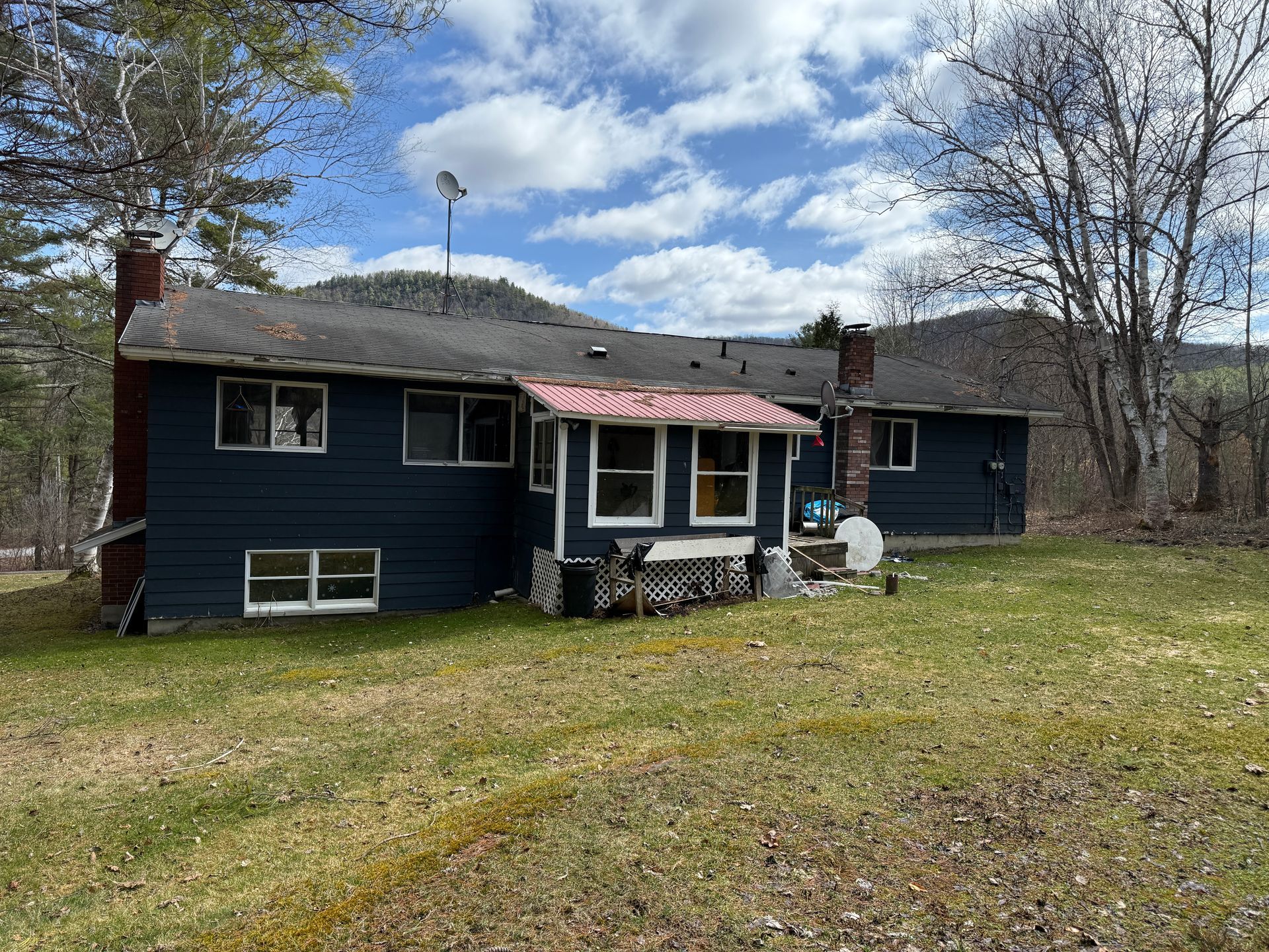Dark blue house with red roof extension and chimneys on a grassy hillside under a cloudy sky.