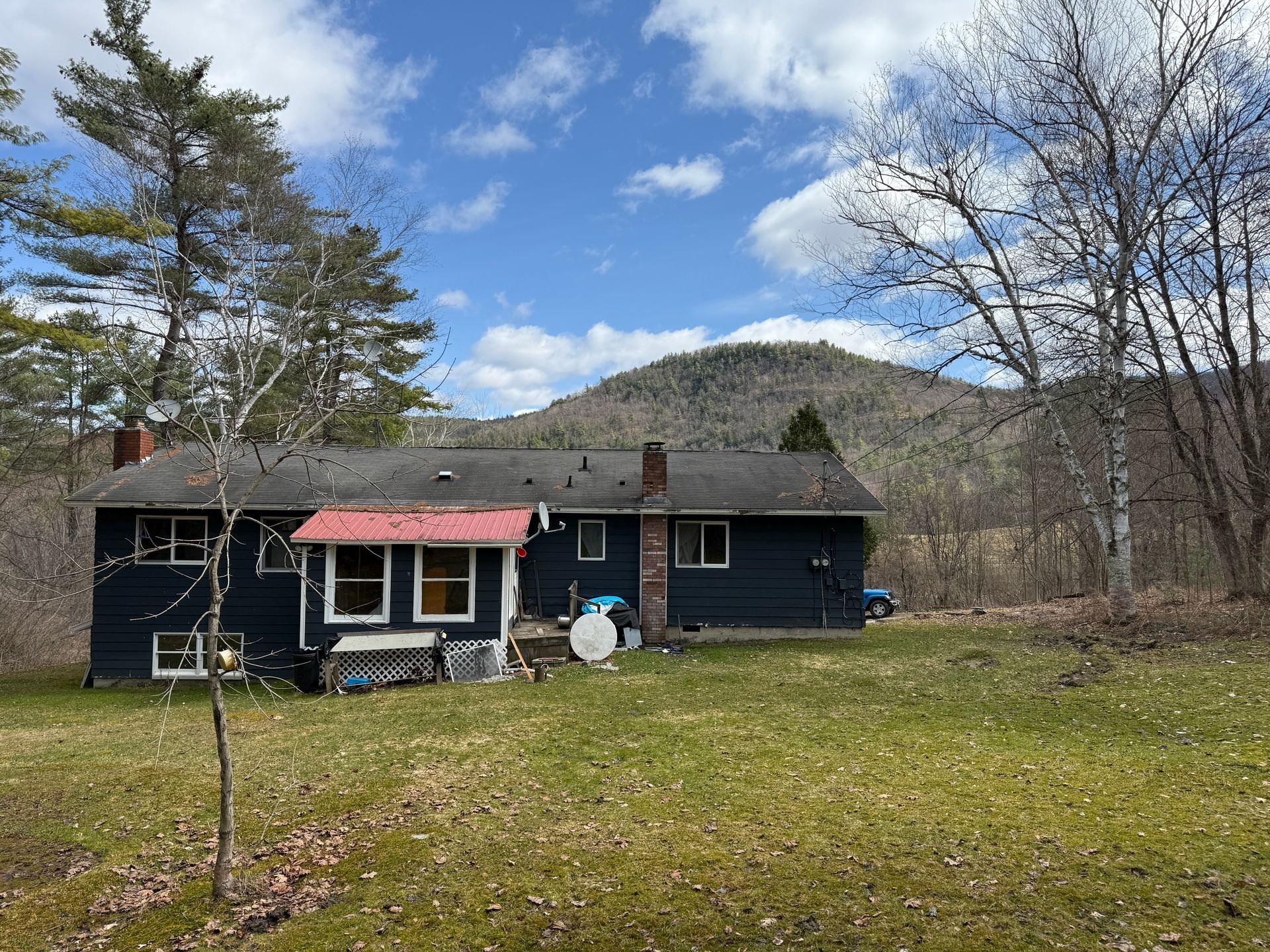 Dark blue house with red awning and two chimneys, in front of a mountain, under a blue sky.
