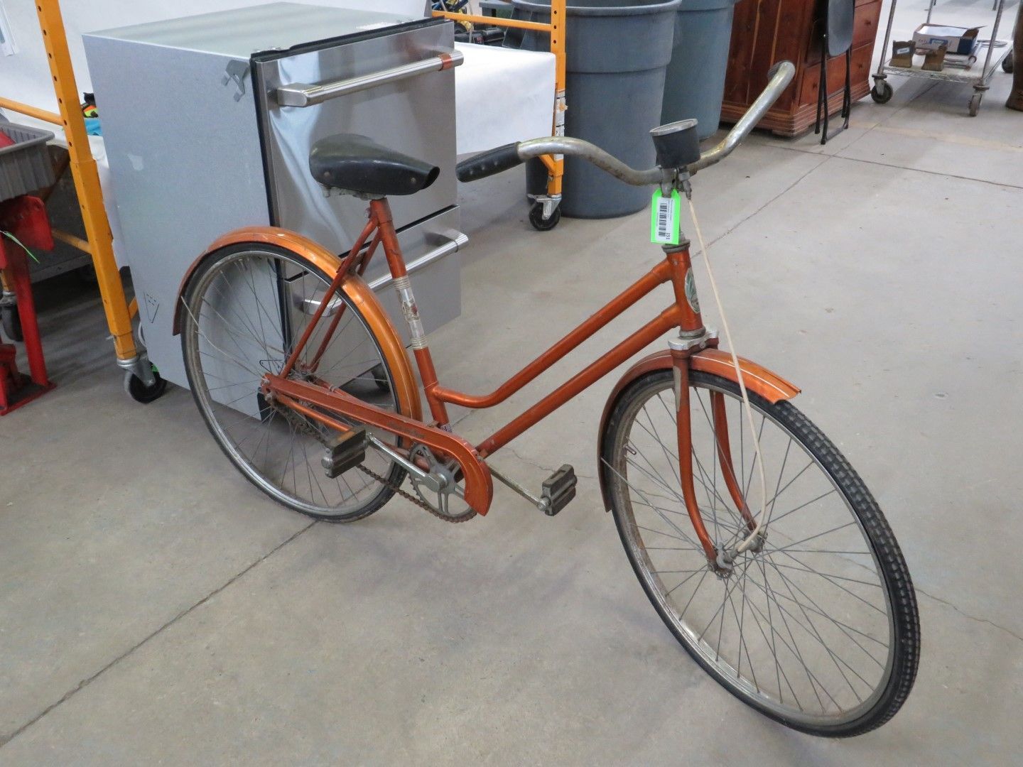 Orange vintage bicycle with black seat and tires in a warehouse.