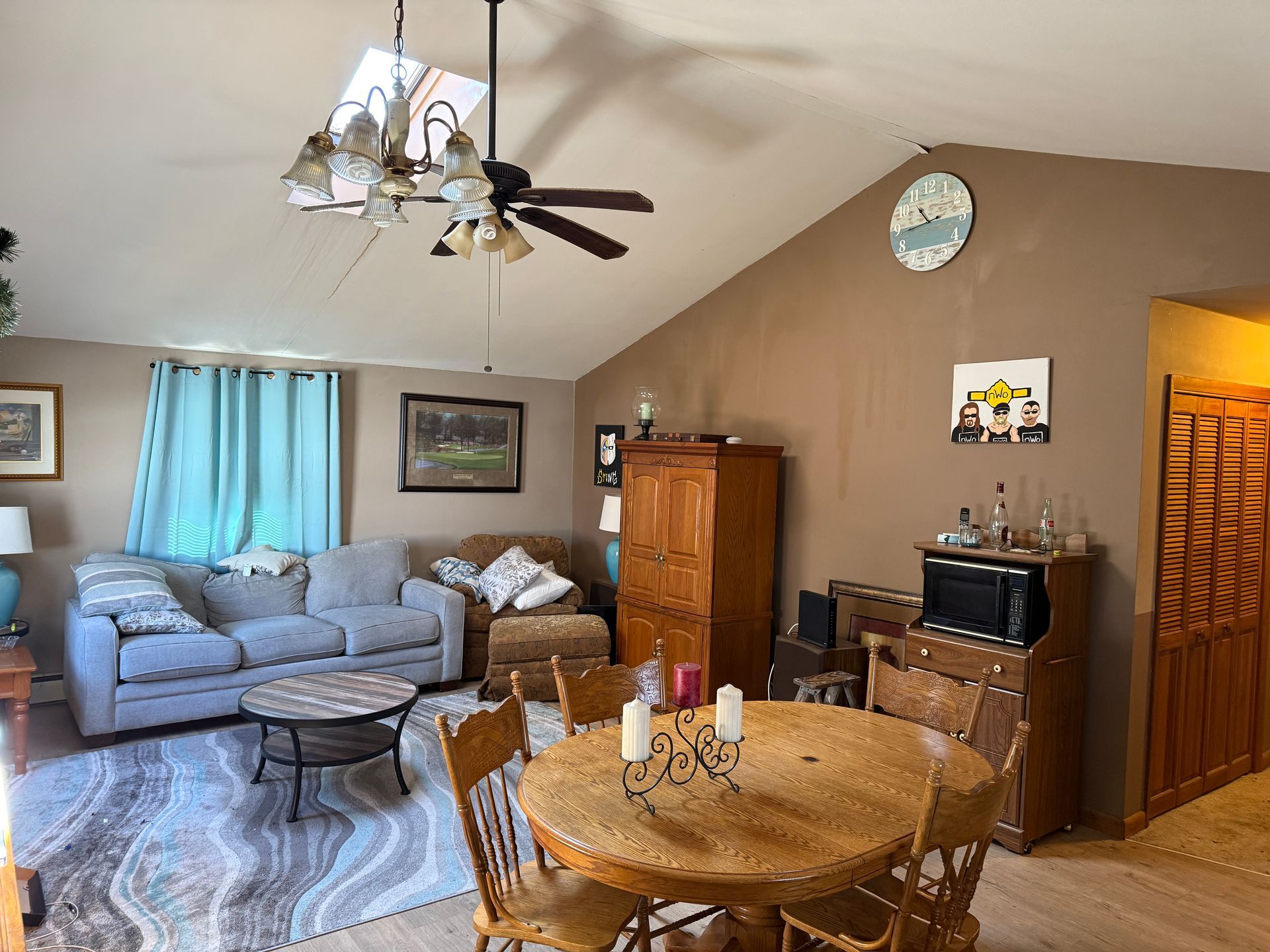 Living room with couch, round table, cabinets, brown walls, and a ceiling fan.