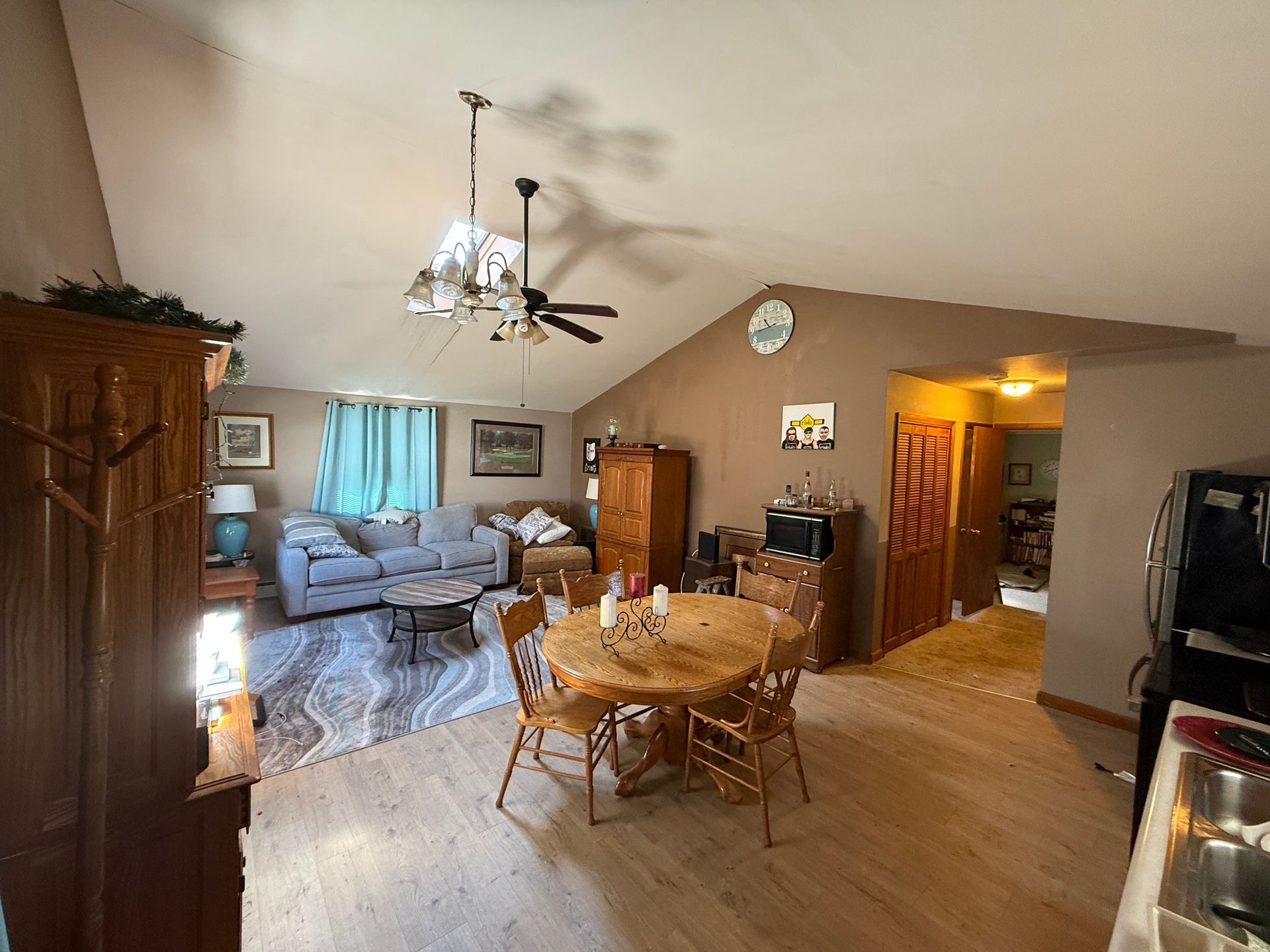 Living room with couch, dining table, and brown walls. Sunlight streams in.