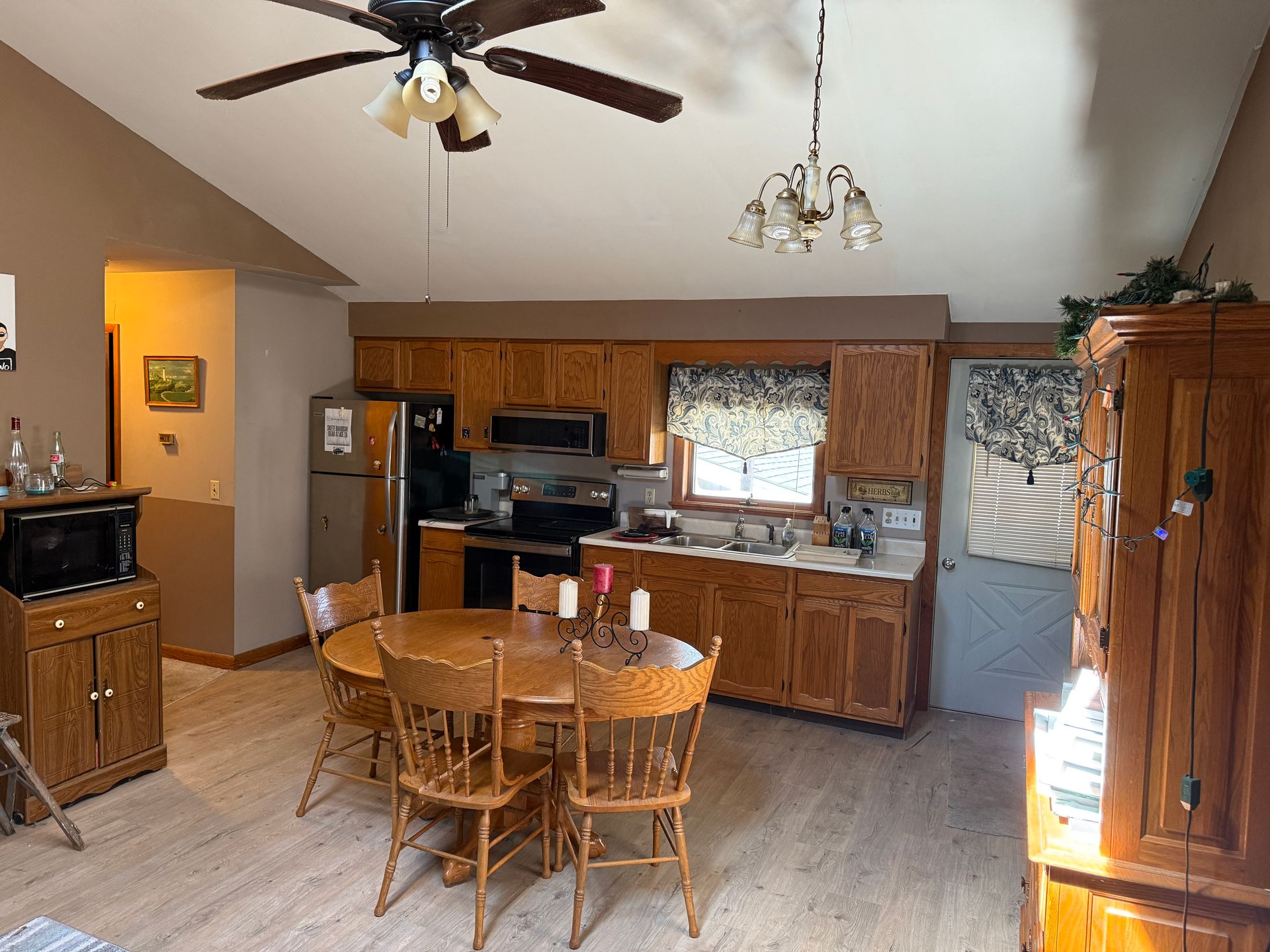 Kitchen with wooden cabinets, round table and chairs, microwave, and ceiling fan.