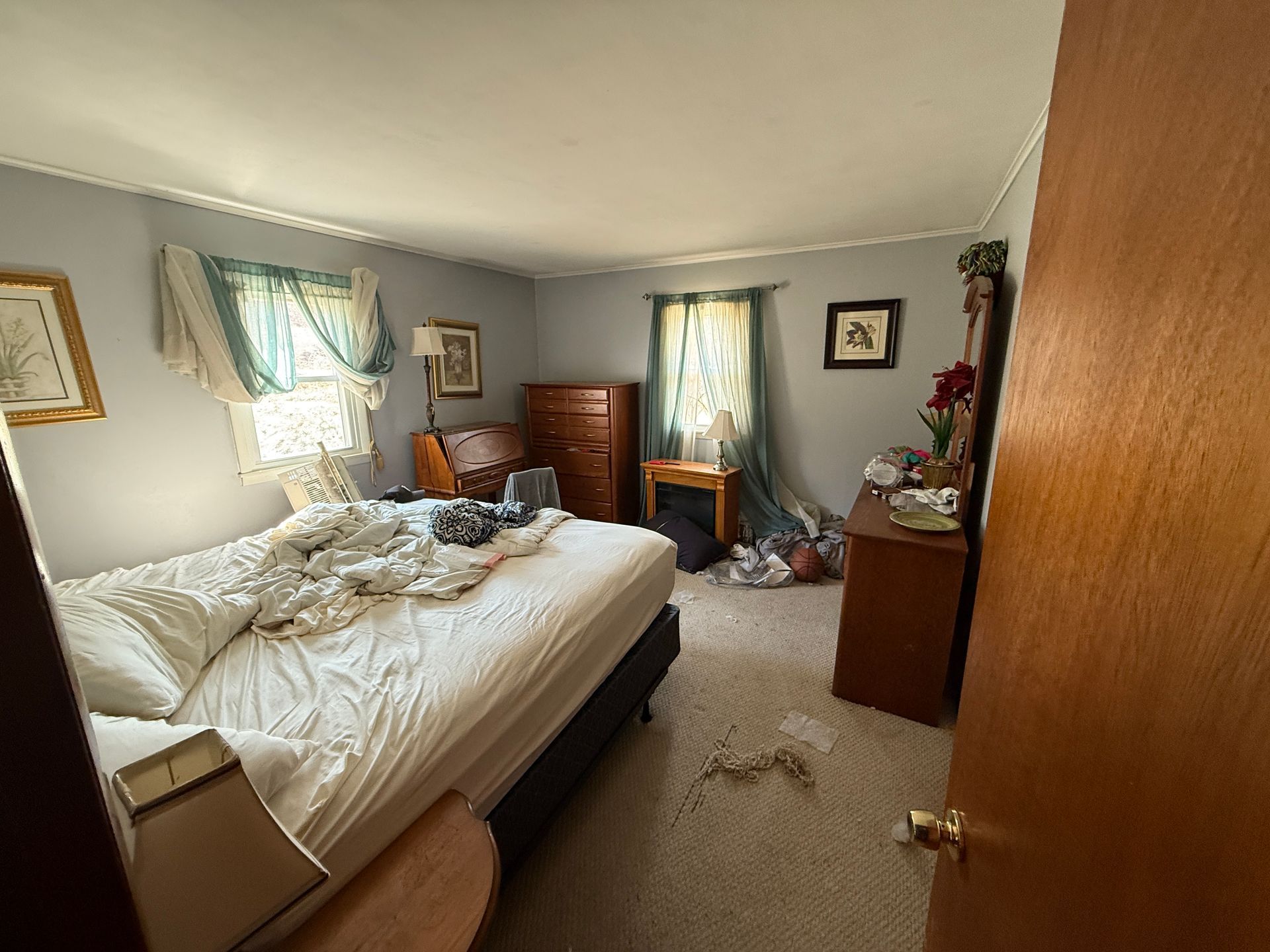 Bedroom with bed, dresser, desk, and gray walls. Window with green curtains.