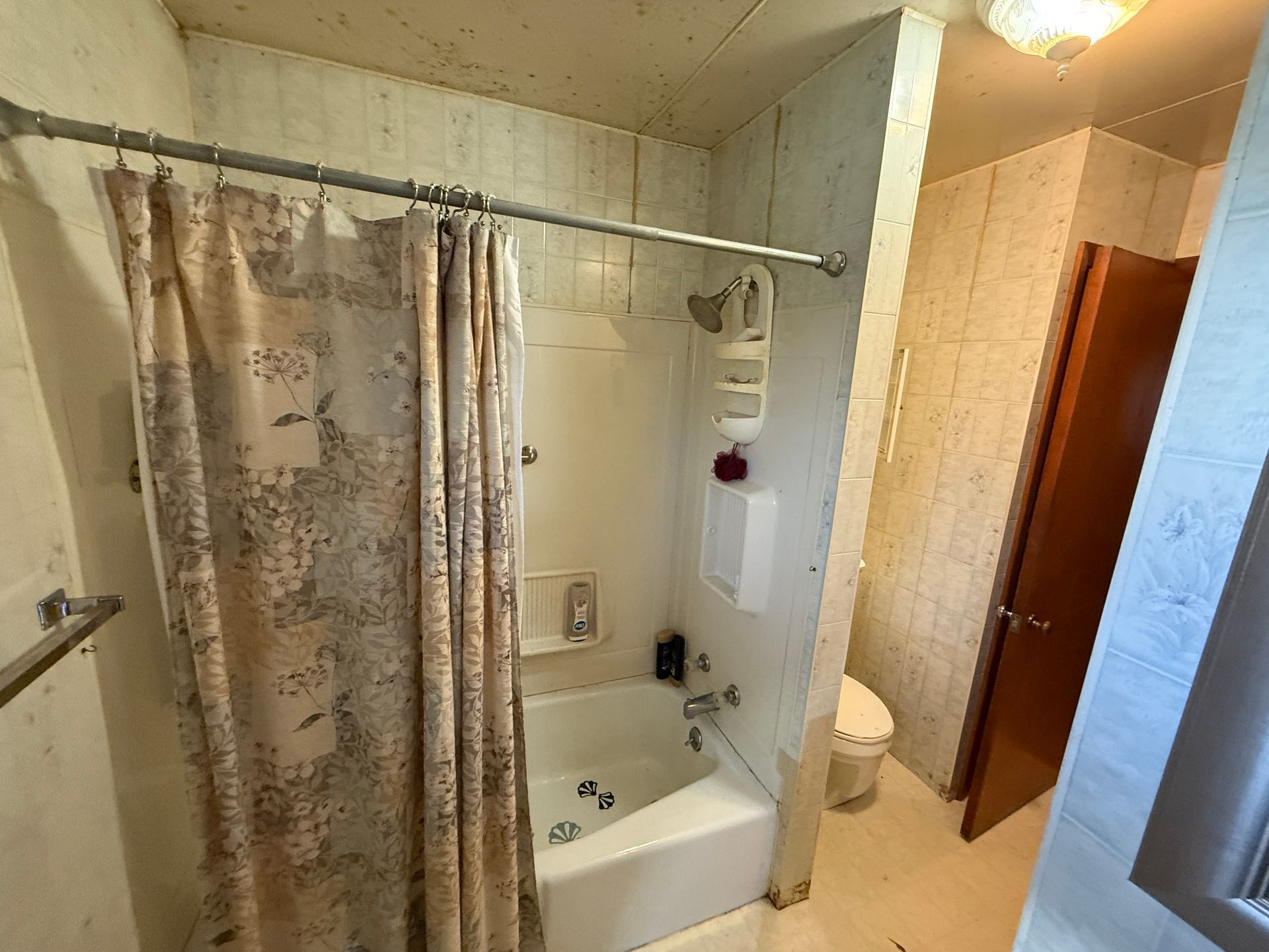 Bathroom with shower/tub, curtain, toilet, and door; light-colored walls and floor.