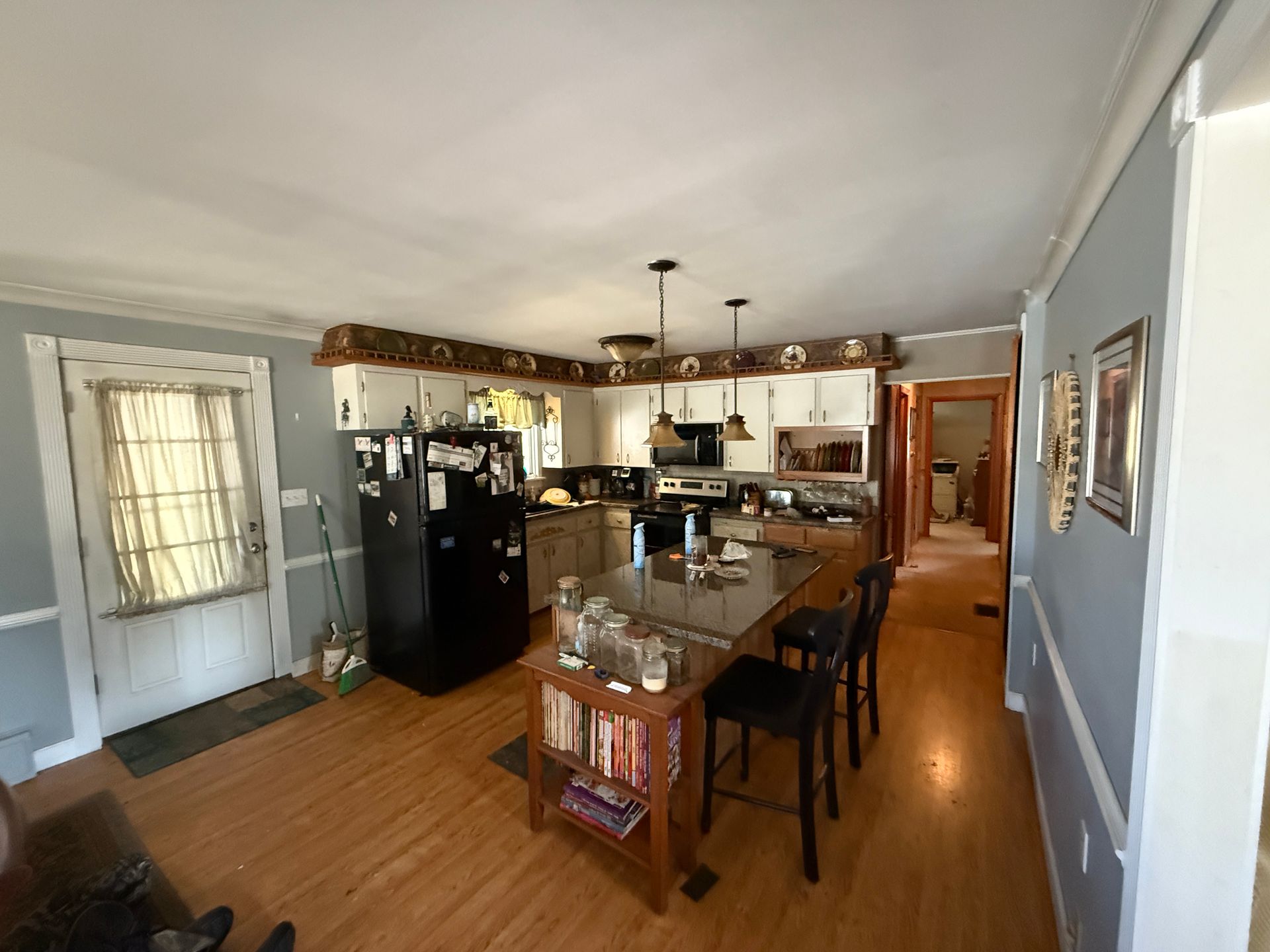 Kitchen with island and black refrigerator. Light wood floors, white cabinets, and blue walls.