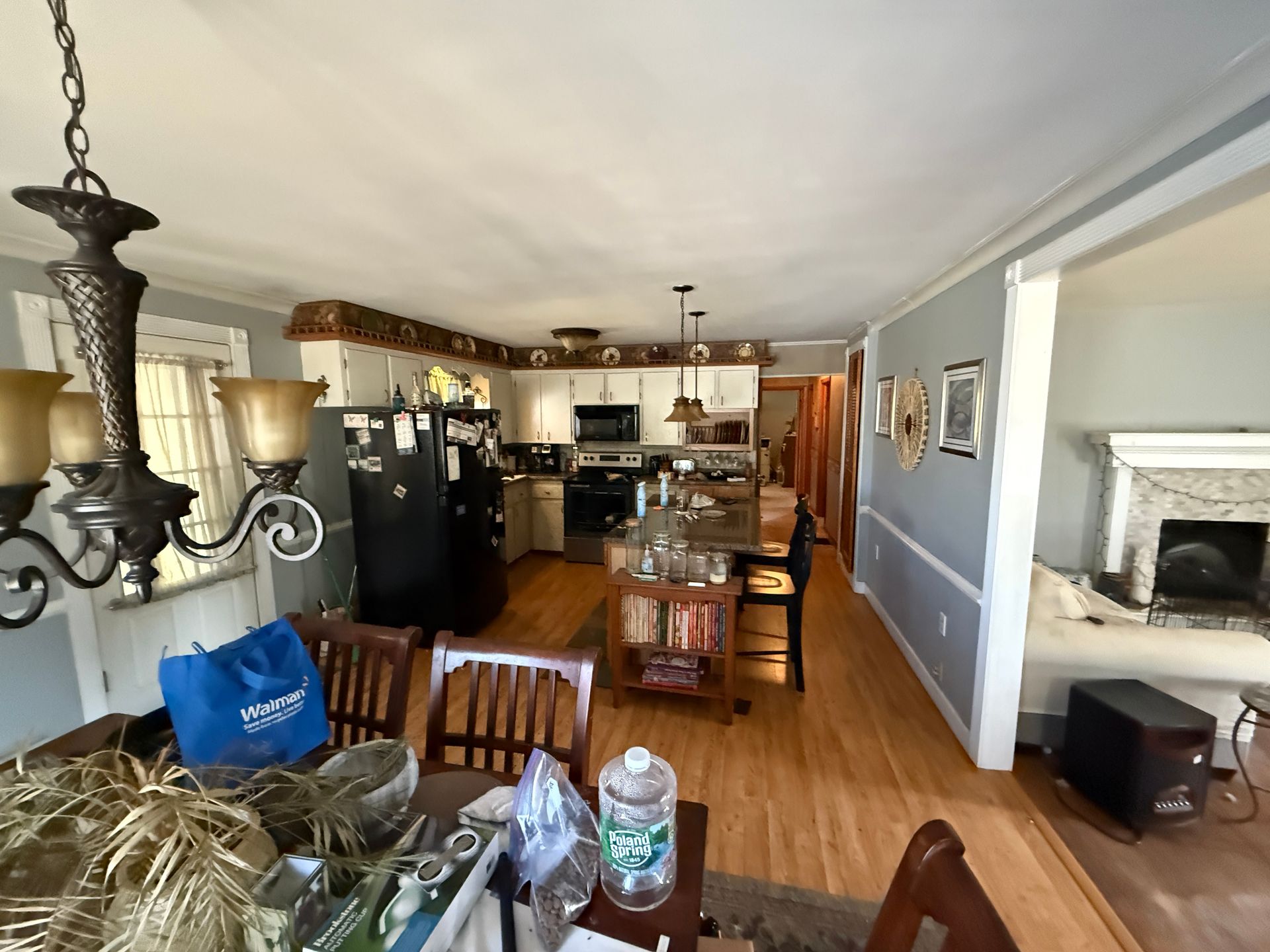 Kitchen with light wood floor, white cabinets, and island. Dining area with chandelier, chairs, and table.