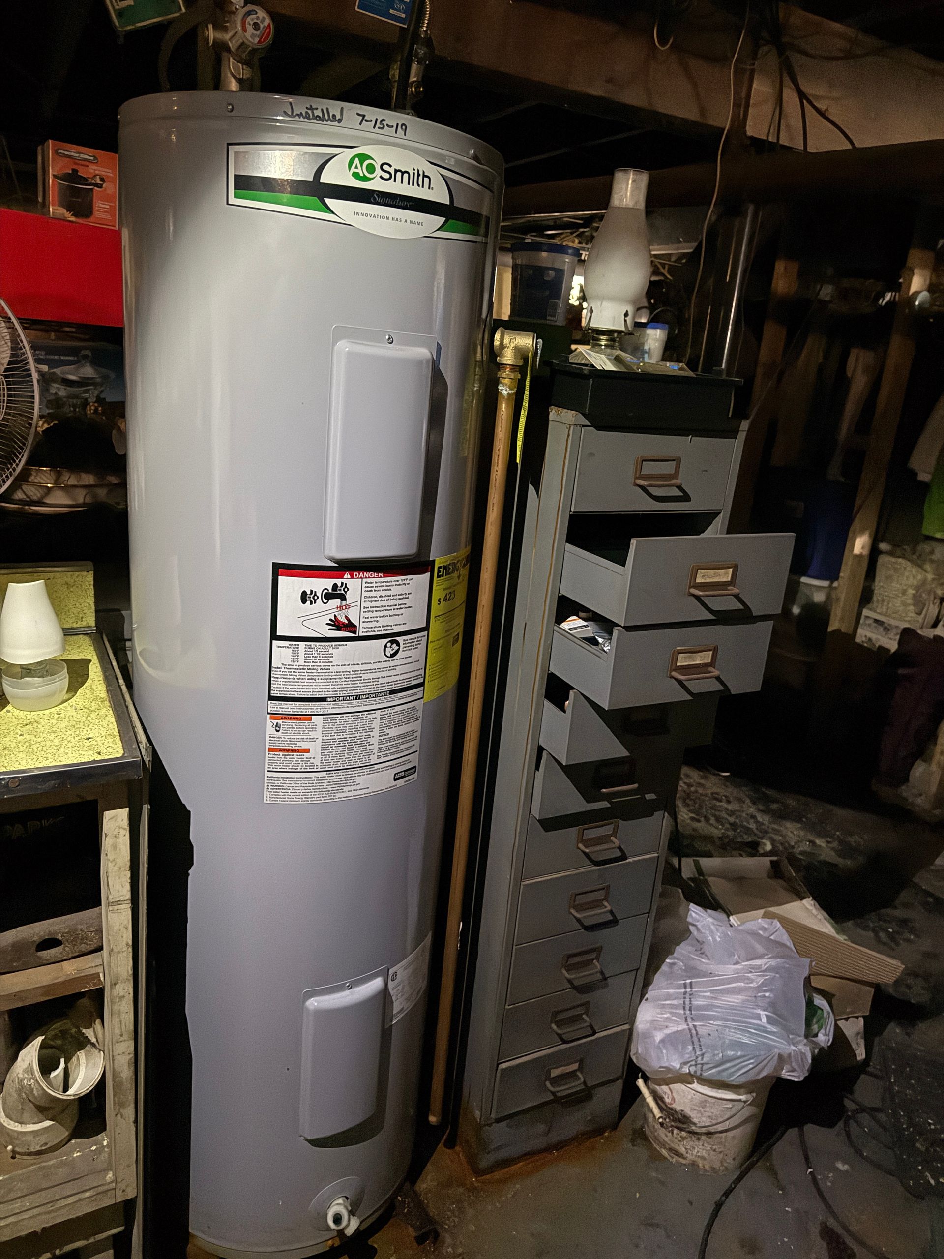 Water heater beside a filing cabinet in a basement.
