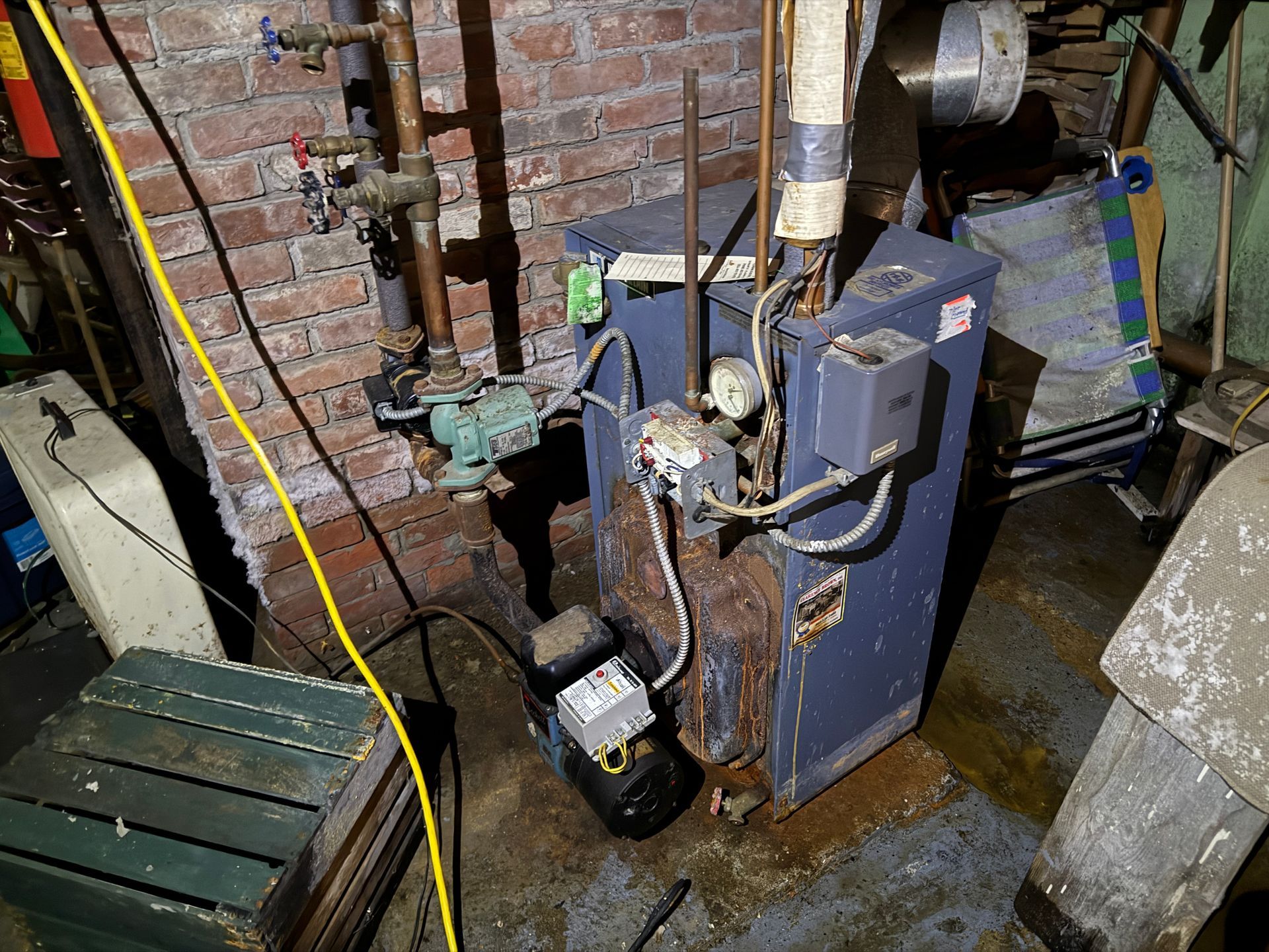 A blue oil-fired boiler in a basement. Copper pipes and brick wall. Black motor sits below.