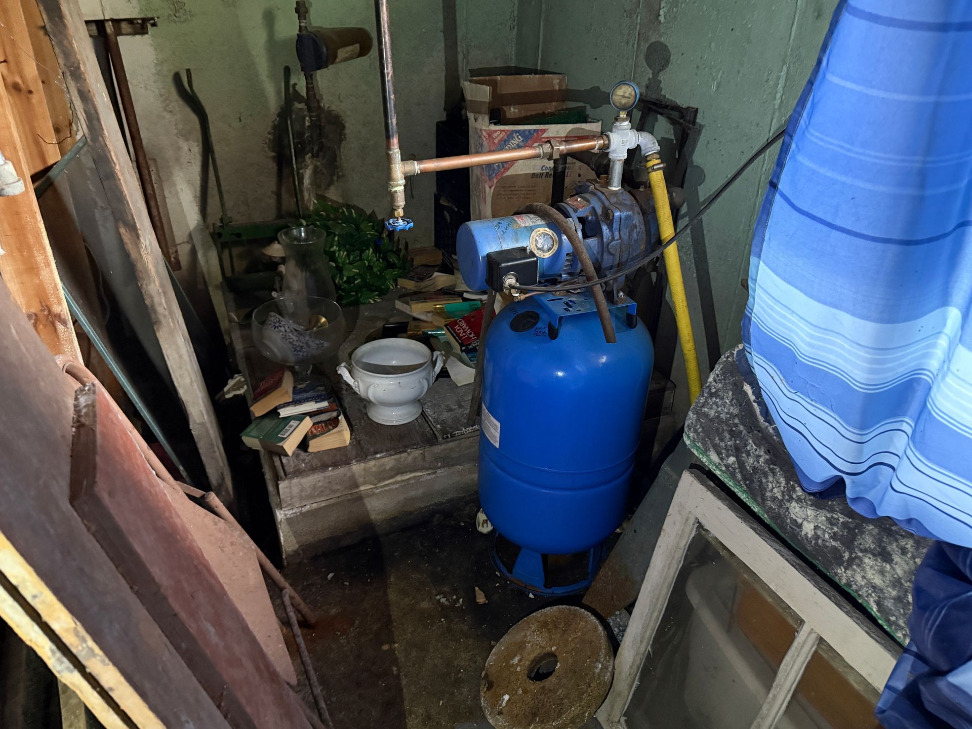 A basement with a blue water tank, pipes, and various stored items.