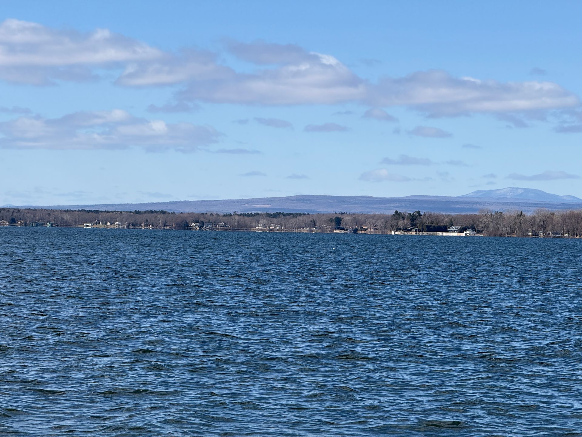 Blue water of a lake under a partly cloudy sky; a distant treeline and mountains.