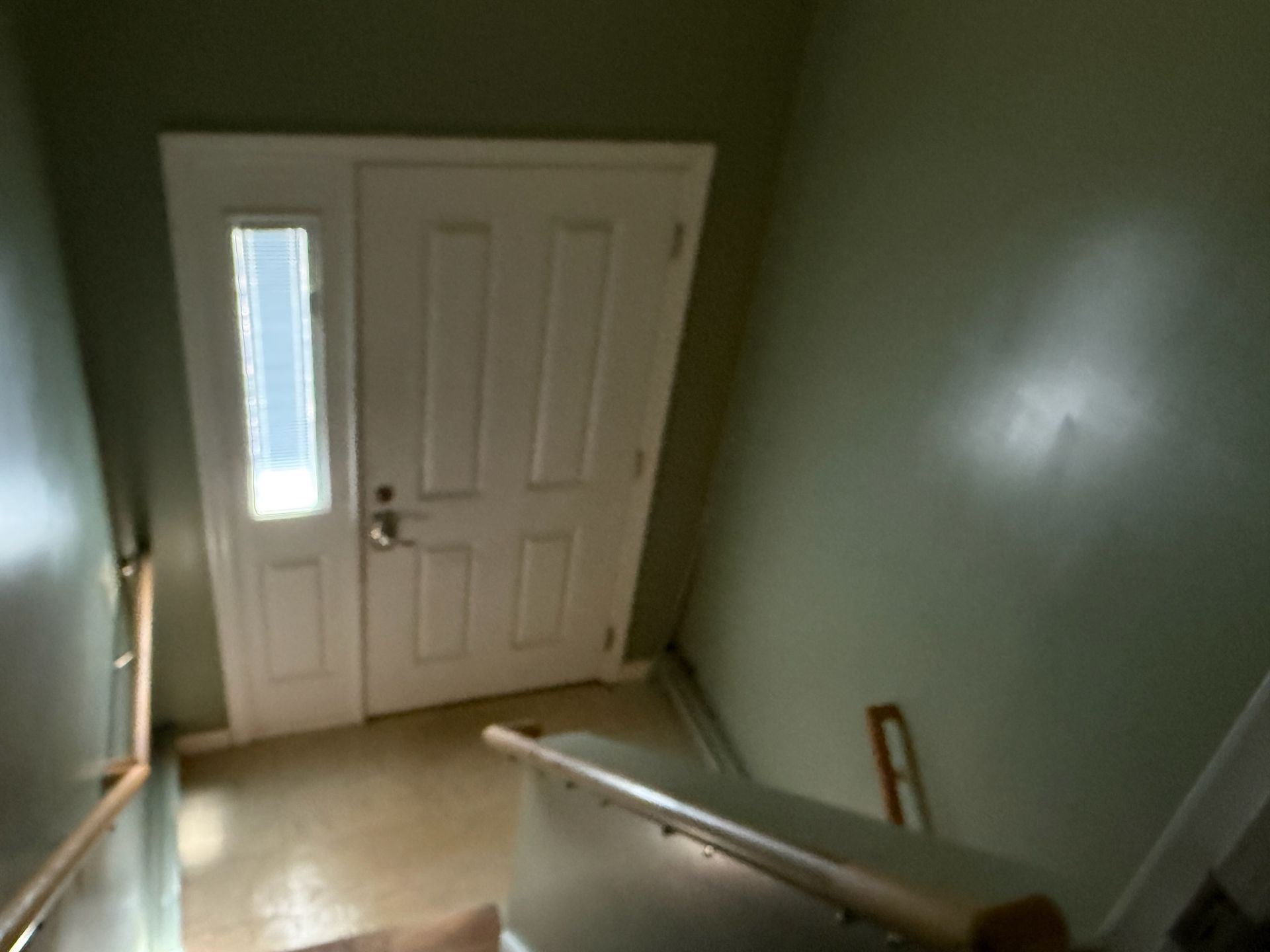 White door with glass panel, leading into a hallway painted green. Staircase with wooden railing is in the foreground.