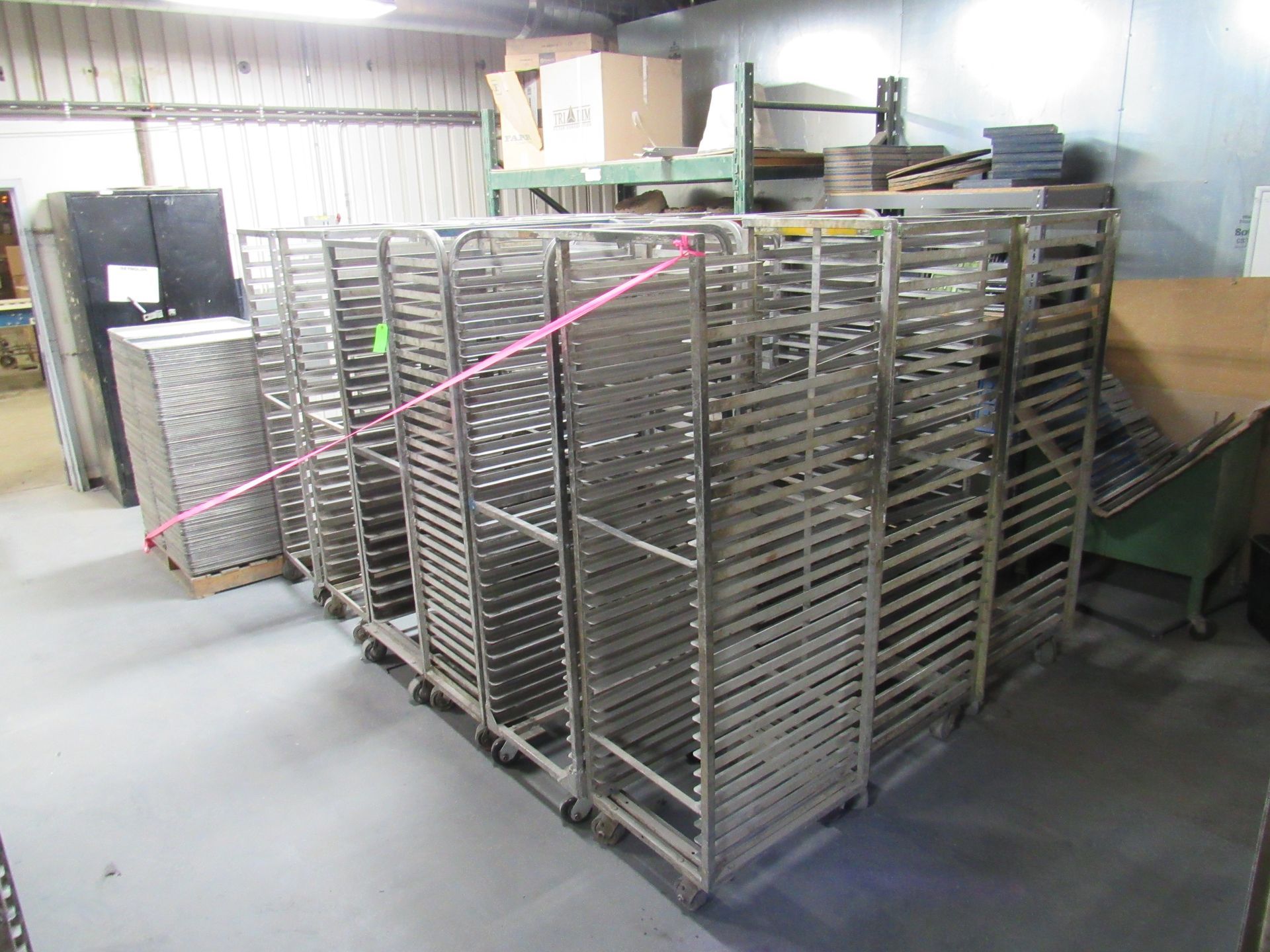 Metal racks on wheels, likely for baking, stacked in a warehouse.