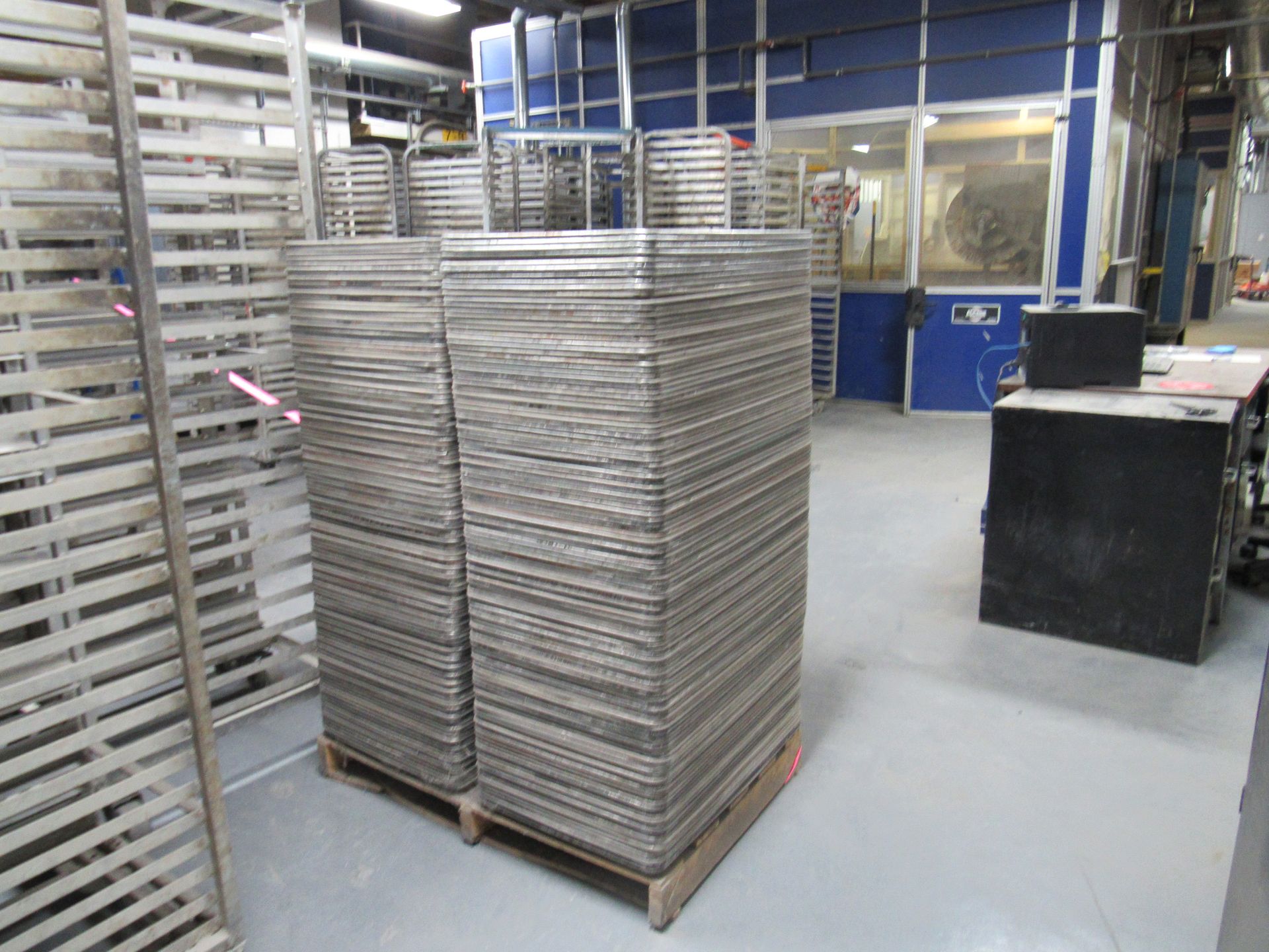 Stacks of metal trays on a wooden pallet in a factory setting.