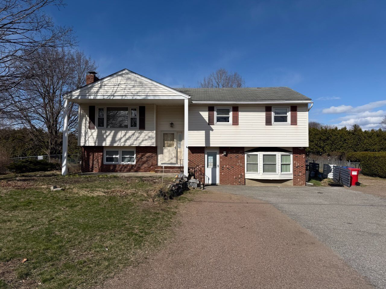 Two-story house with tan siding, red brick base, driveway, and blue sky.