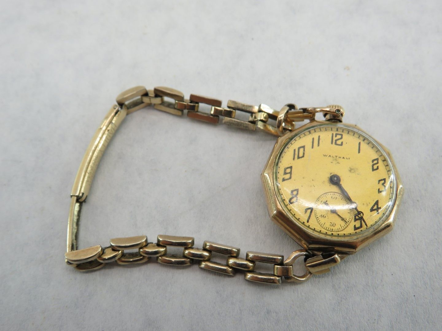 Gold wristwatch with a segmented band and octagonal face, set against a light background.