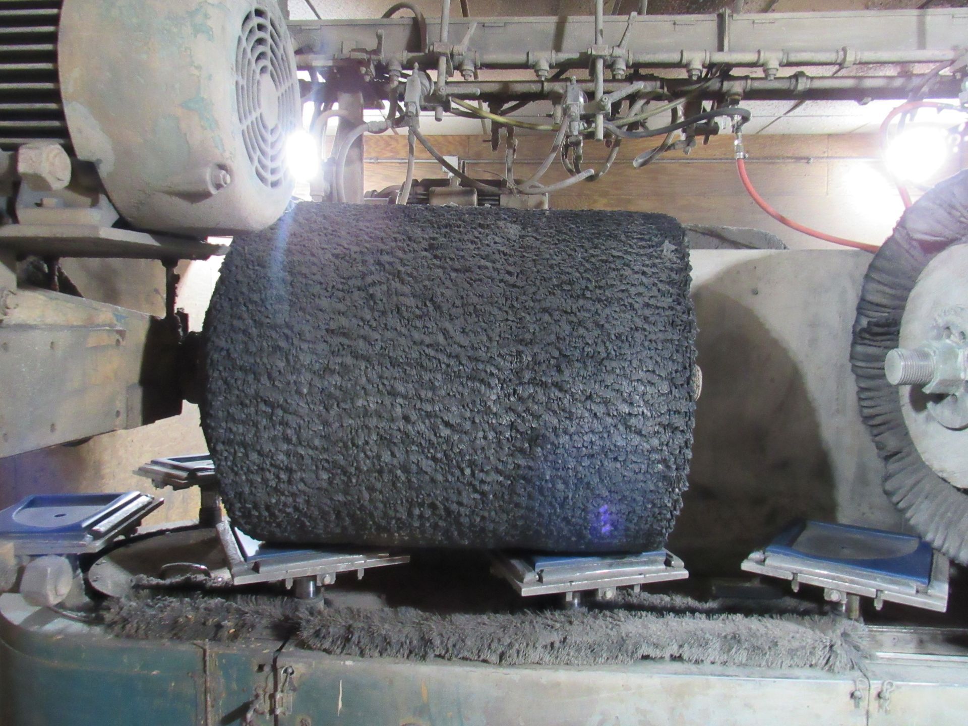 A cylindrical stone grinding machine smoothing a dark, textured stone block in a factory setting.