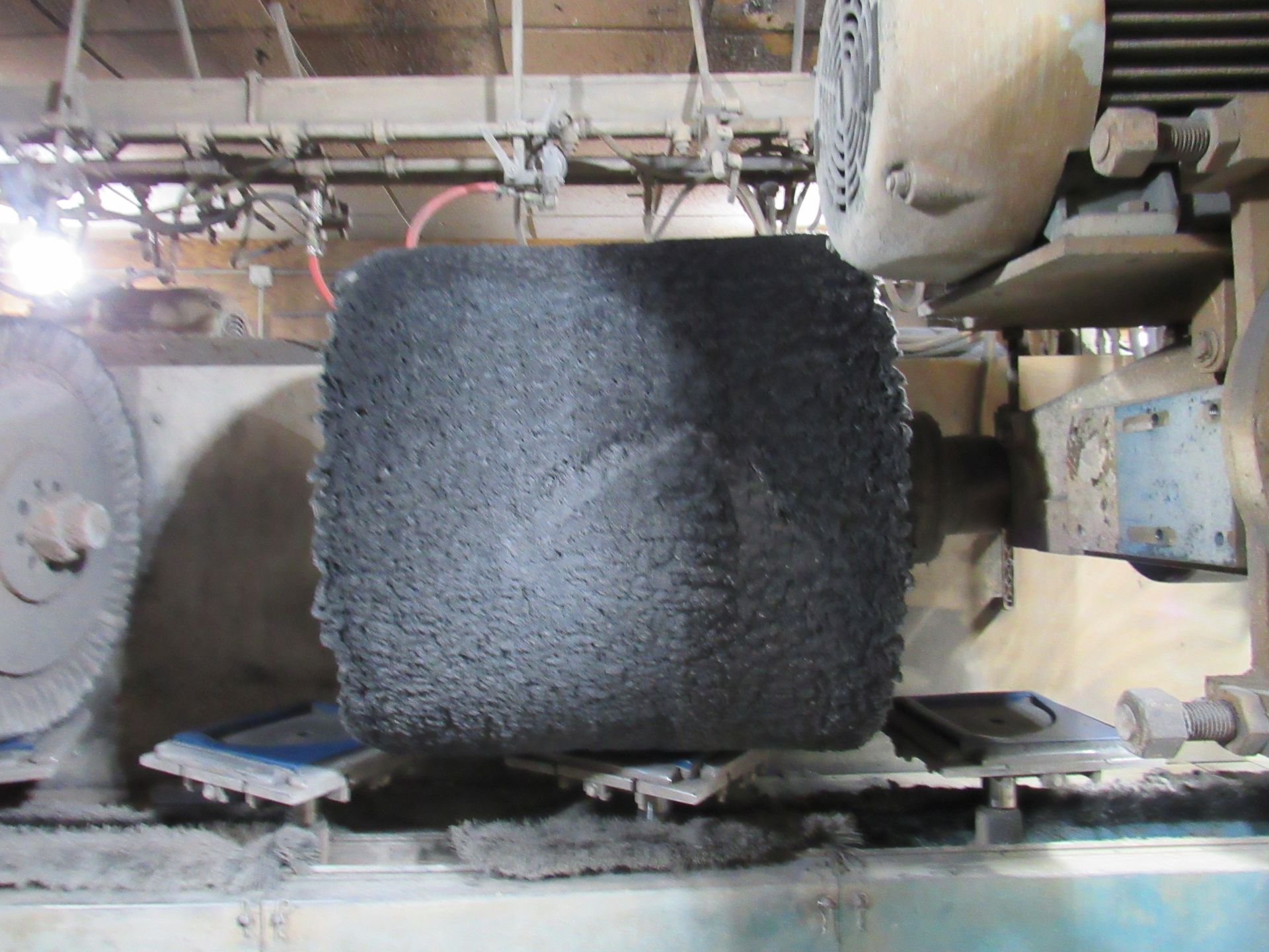 Square, dark-colored stone block on a grinding machine. Industrial setting.