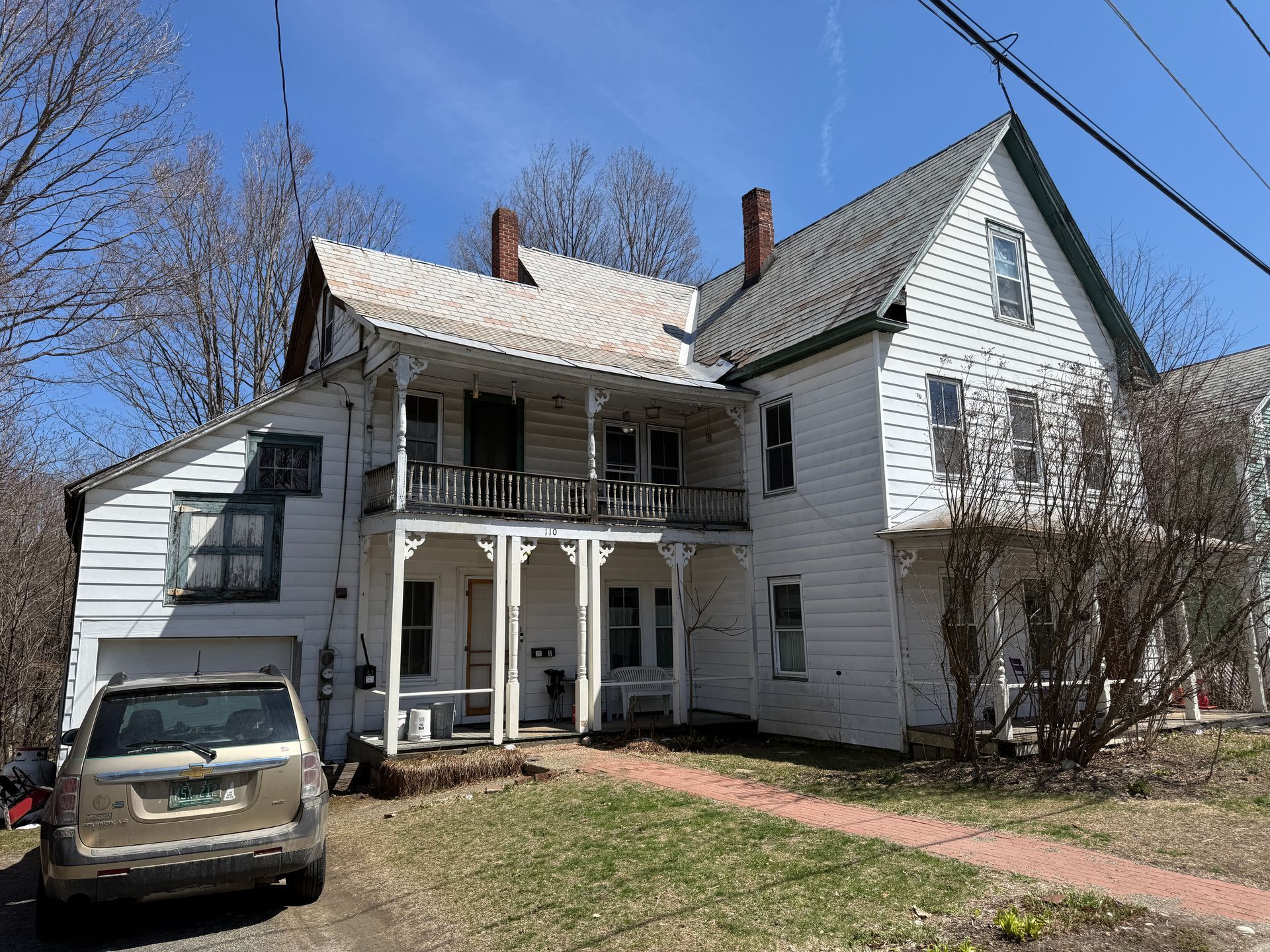 White multi-story house with front porch and parked car in front.
