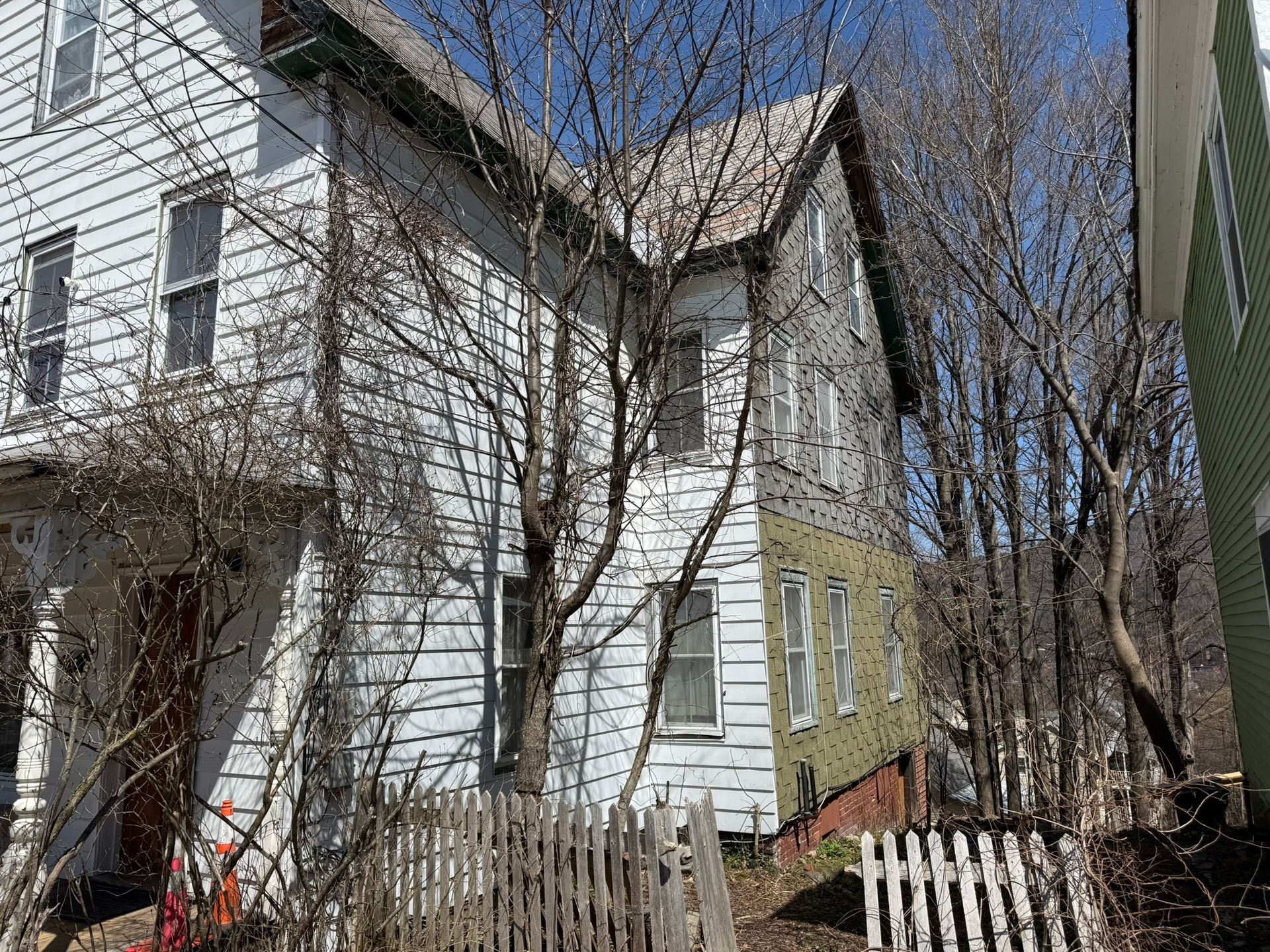 Three-story house with white and green siding; bare trees in front.