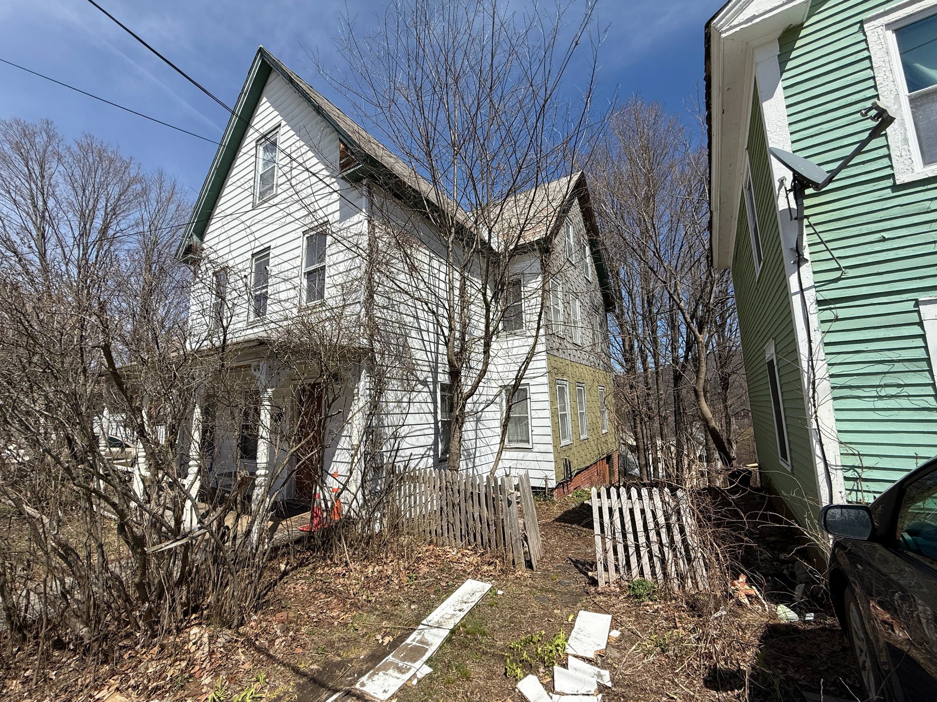 Two-story white house with green trim, wooden fence.