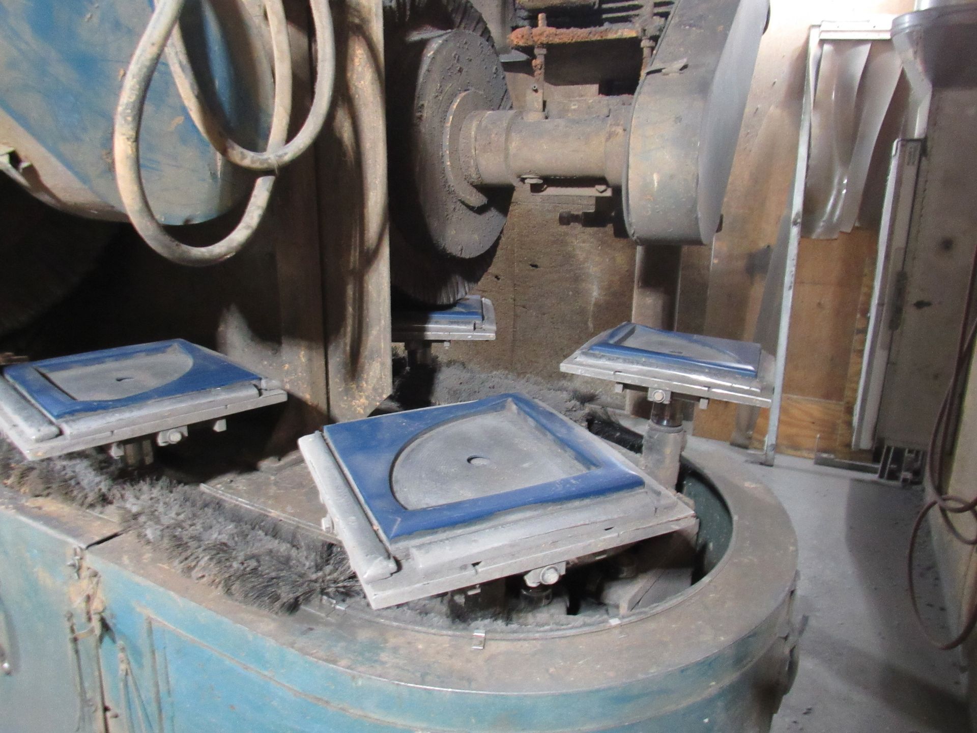 A blue industrial grinder machine with multiple workpieces clamped onto rotating platforms.