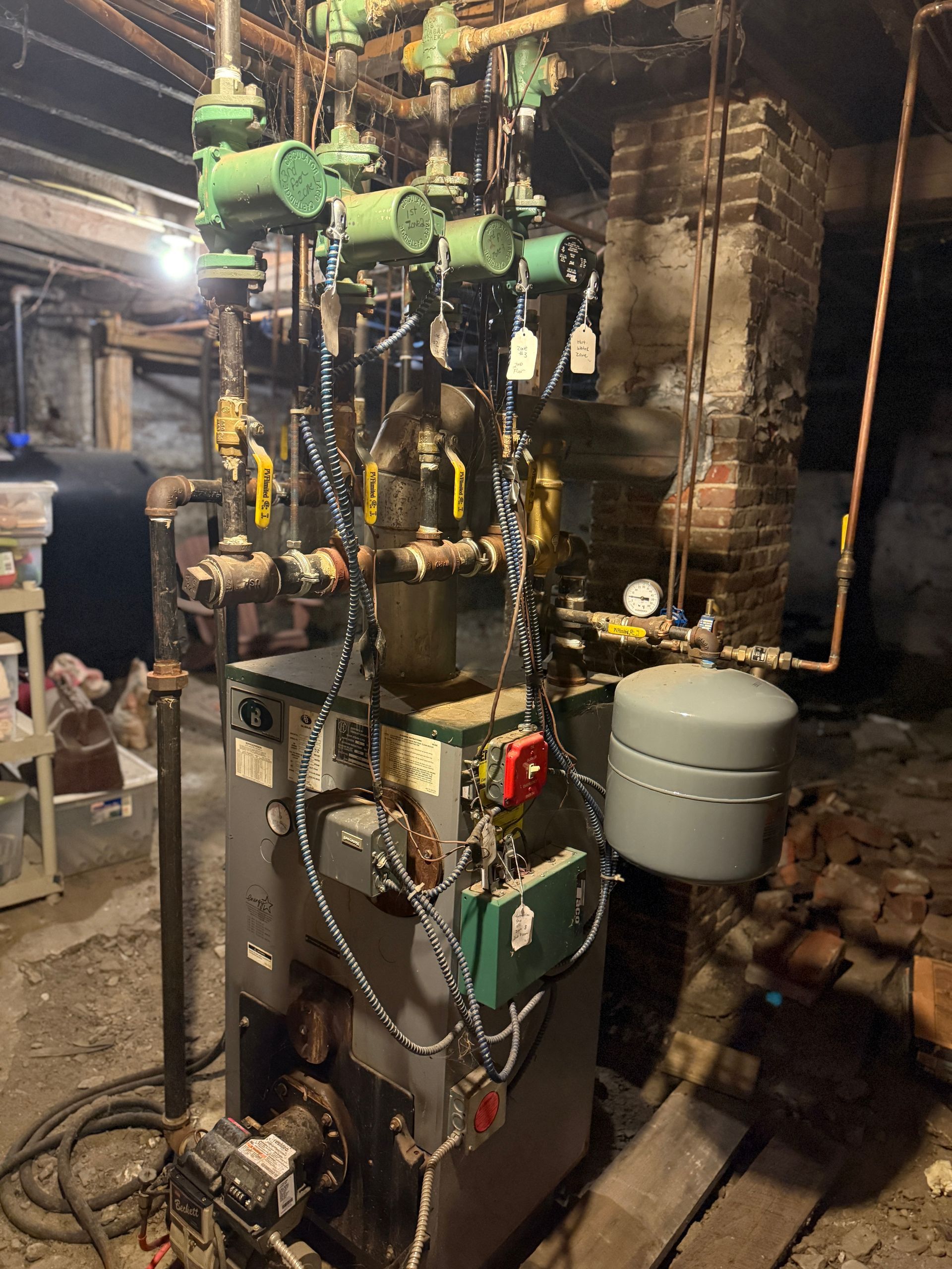 A furnace in a basement with pipes, valves, and an expansion tank.