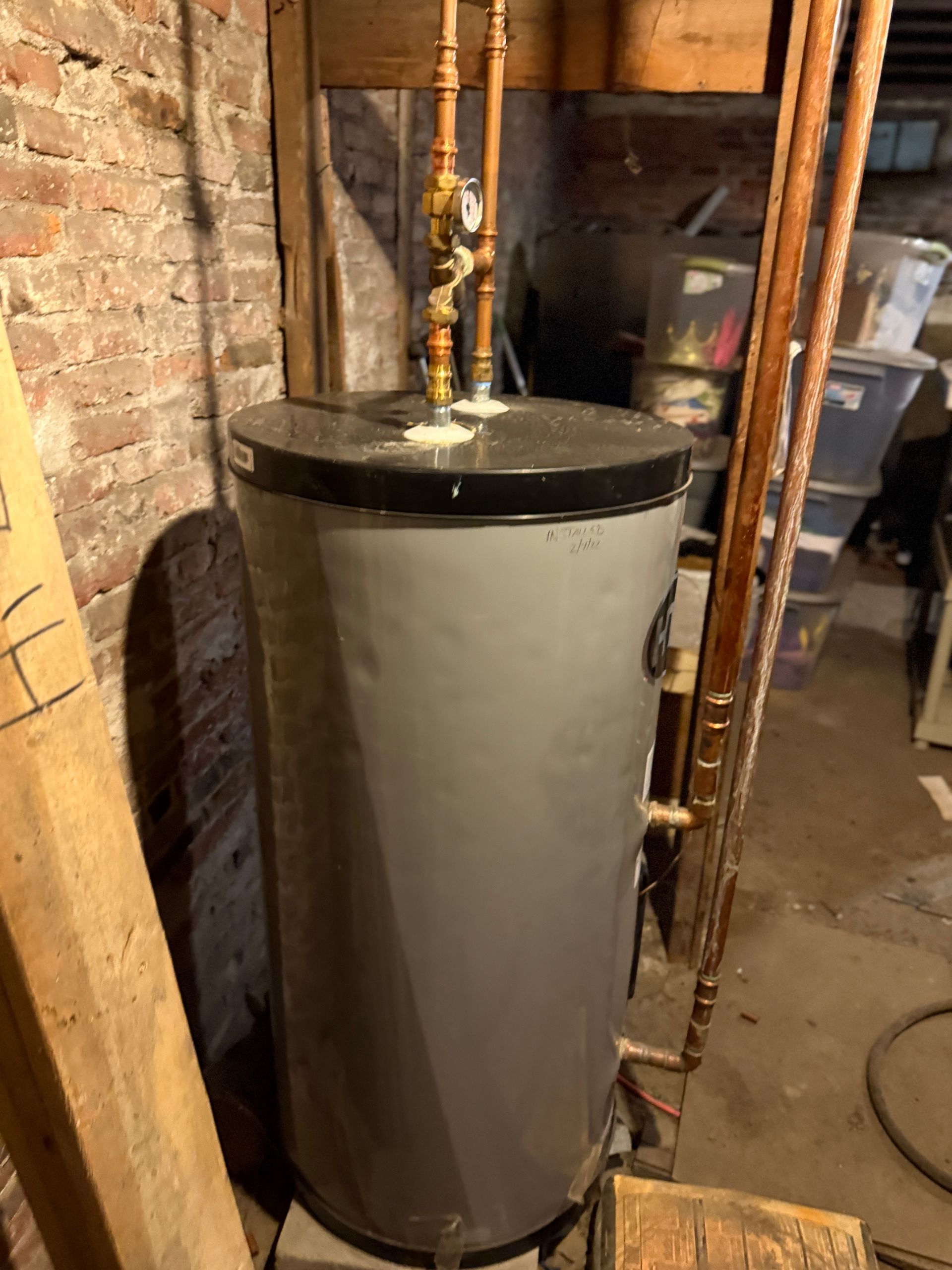 Gray water heater with copper pipes in a basement setting.