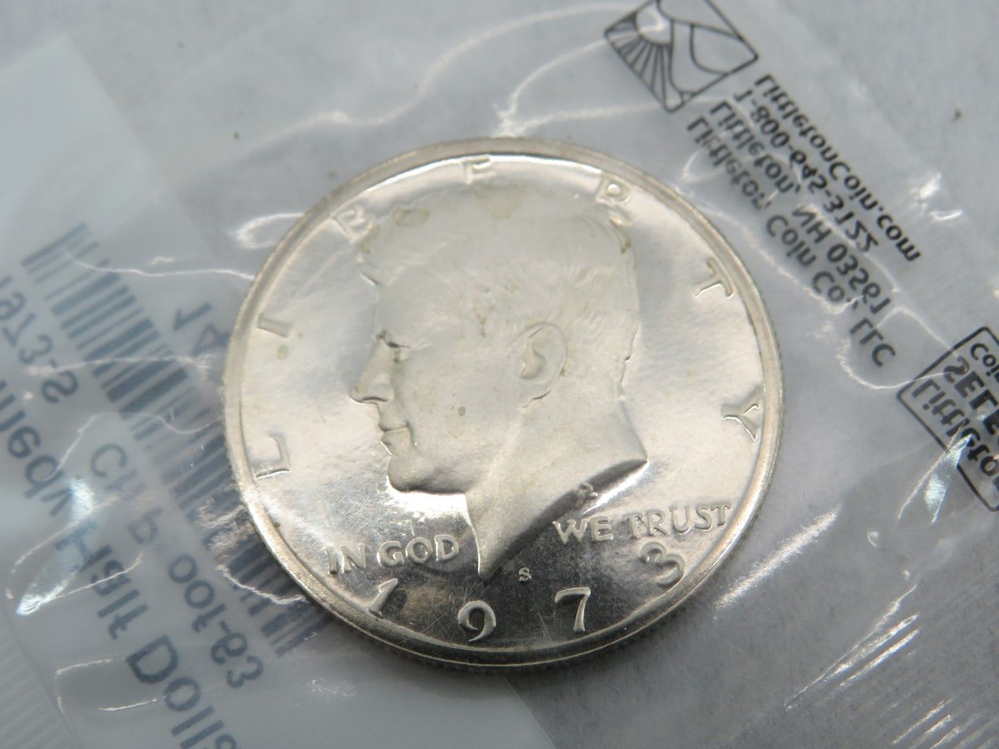 A Kennedy half dollar coin, silver in color, from 1971, inside a plastic bag.
