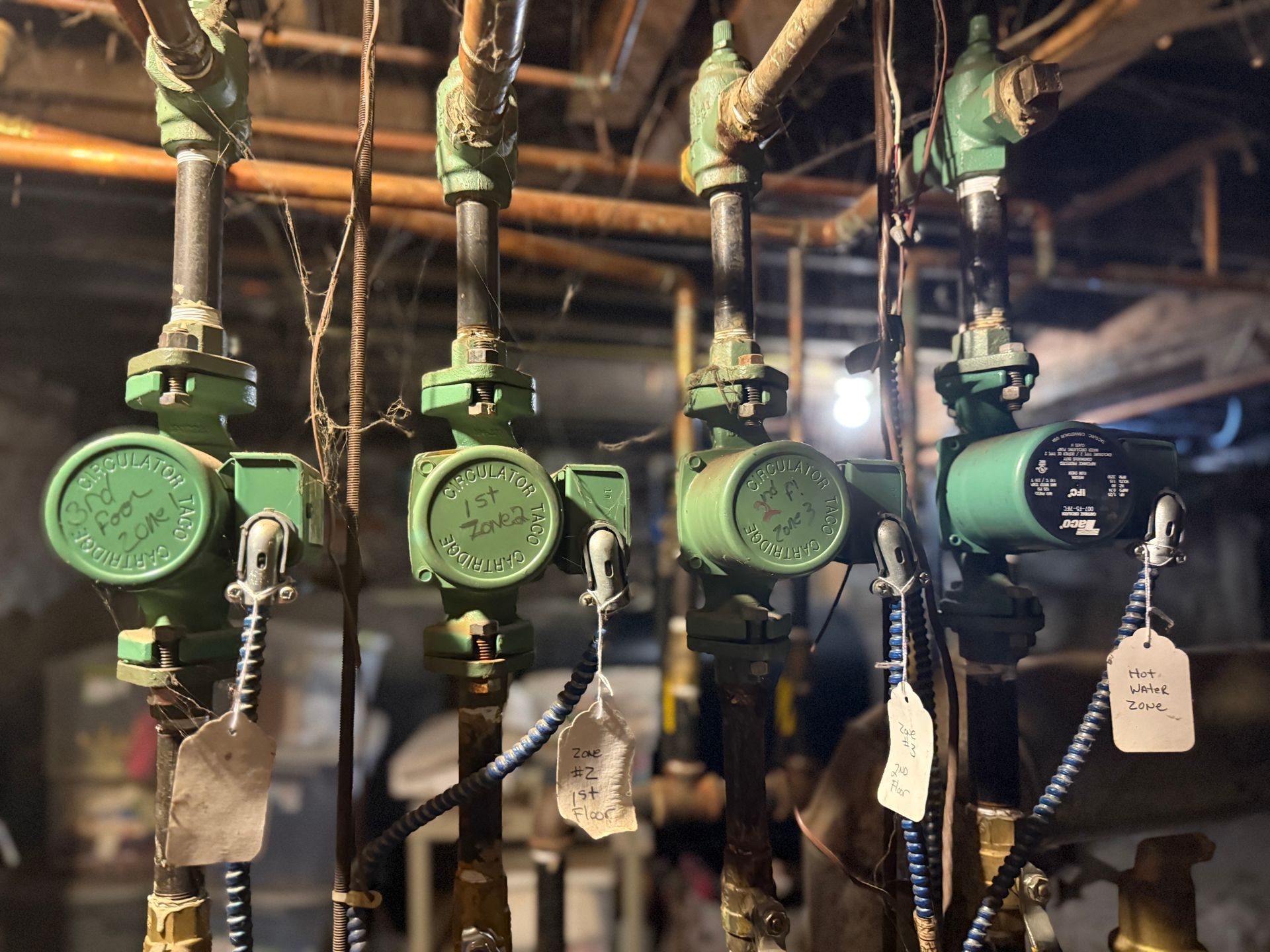 Green pumps and pipes in a basement. Some pumps have hanging tags.