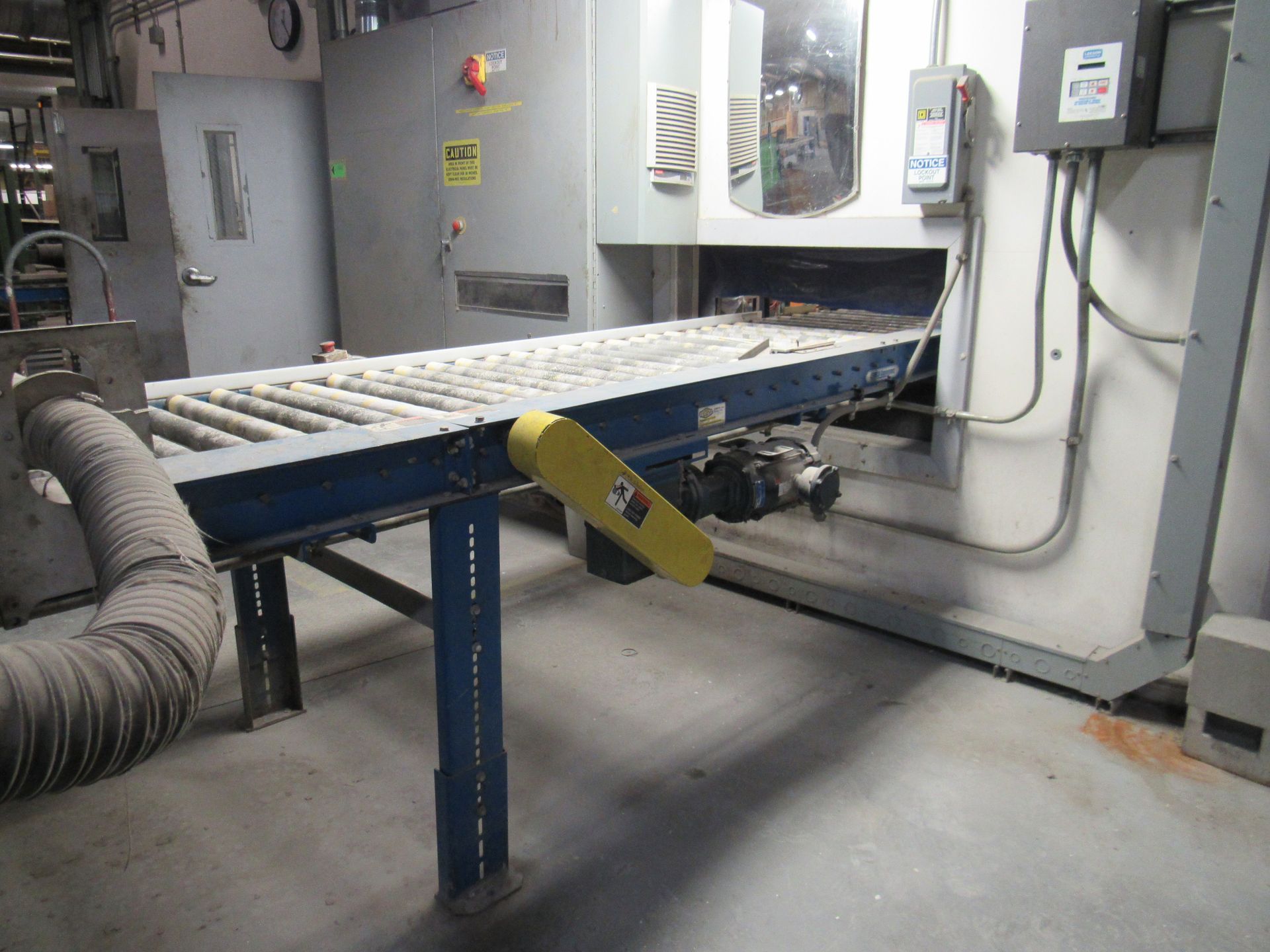 Conveyor belt extending from a large gray machine, inside an industrial setting.