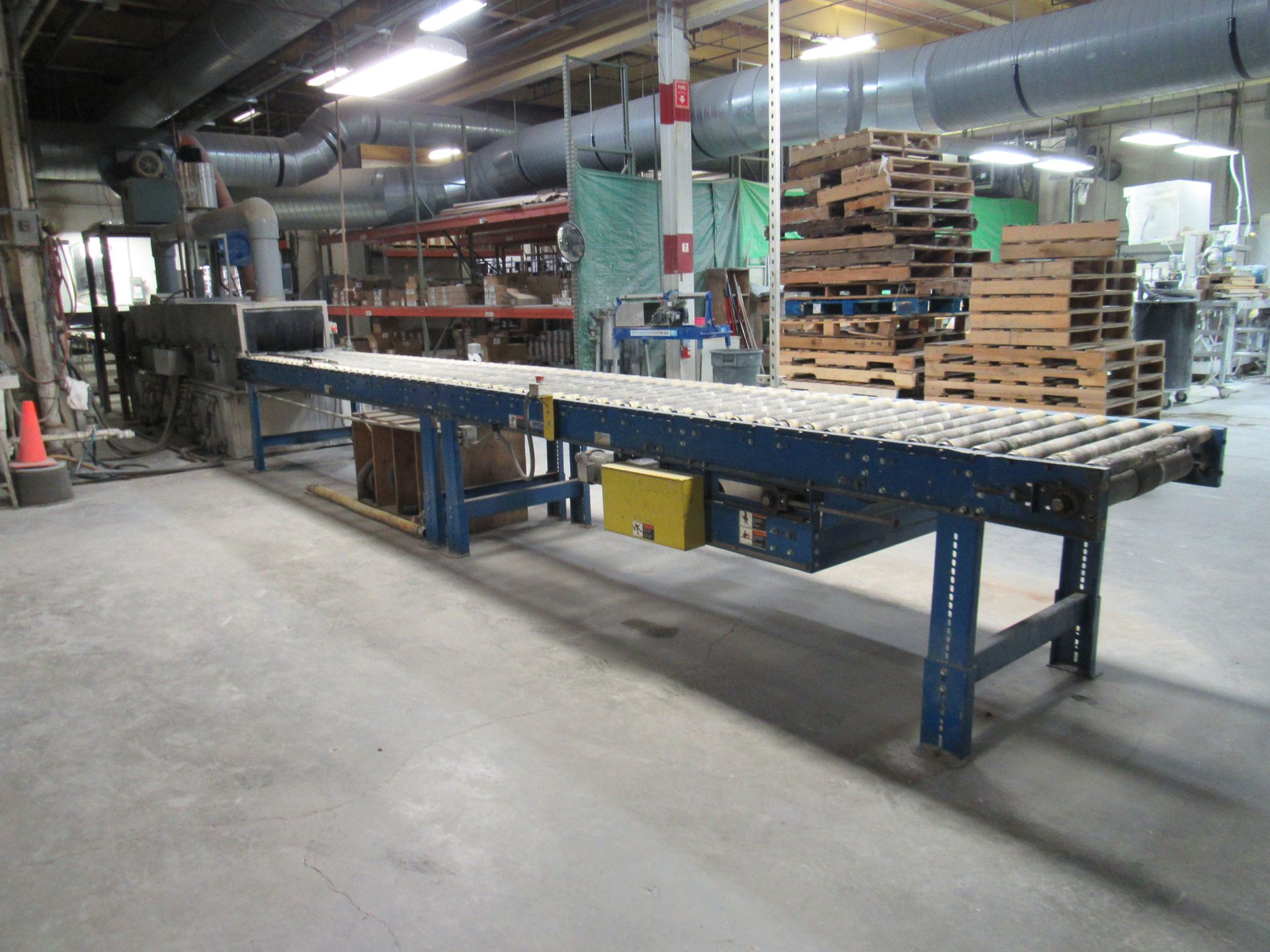 Conveyor belt in a factory setting, transporting items. Gray concrete floor, blue metal supports, and industrial equipment.