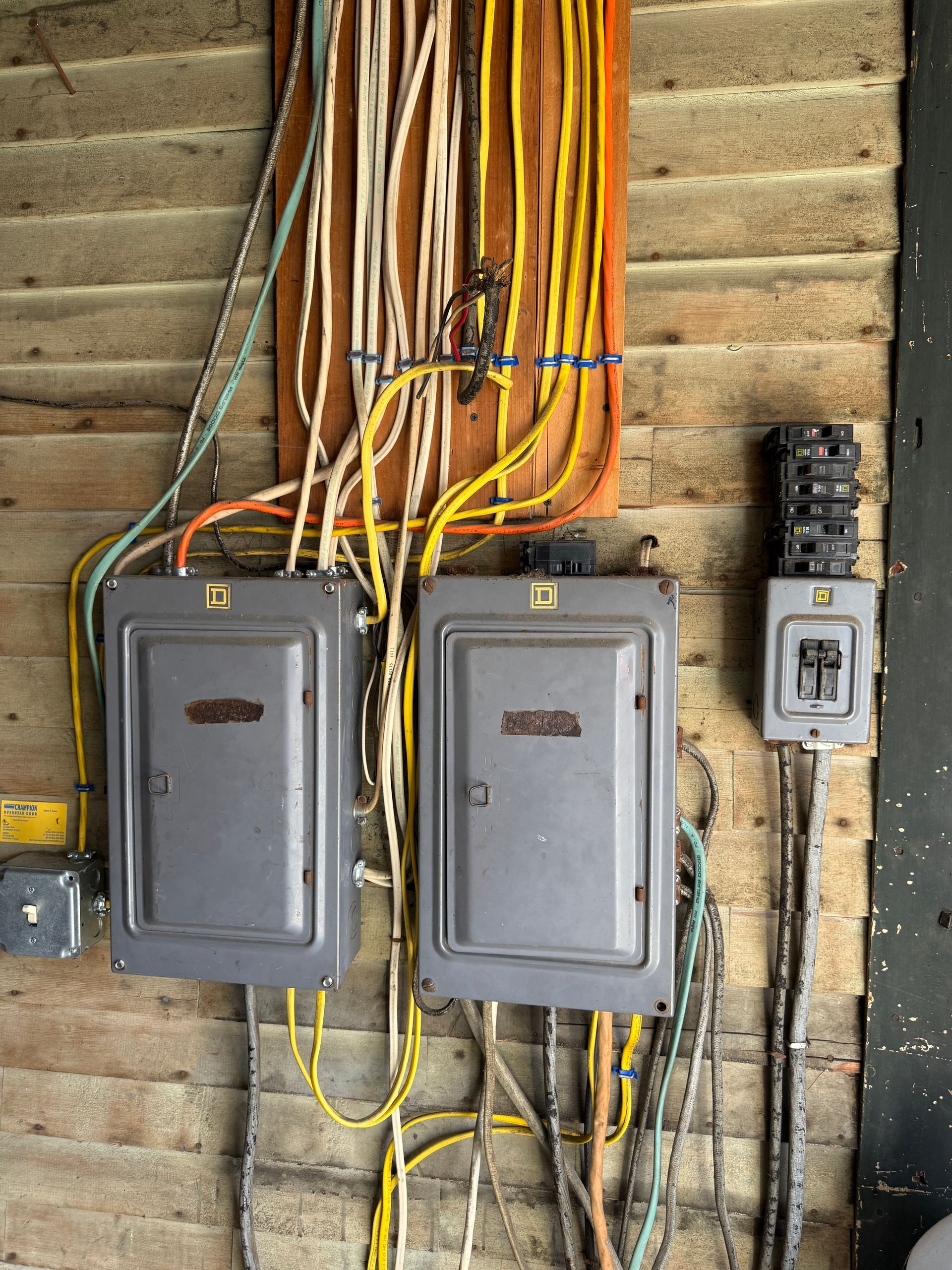Electrical panel boxes with wiring on a wood surface. Yellow, white, and orange cables are visible.