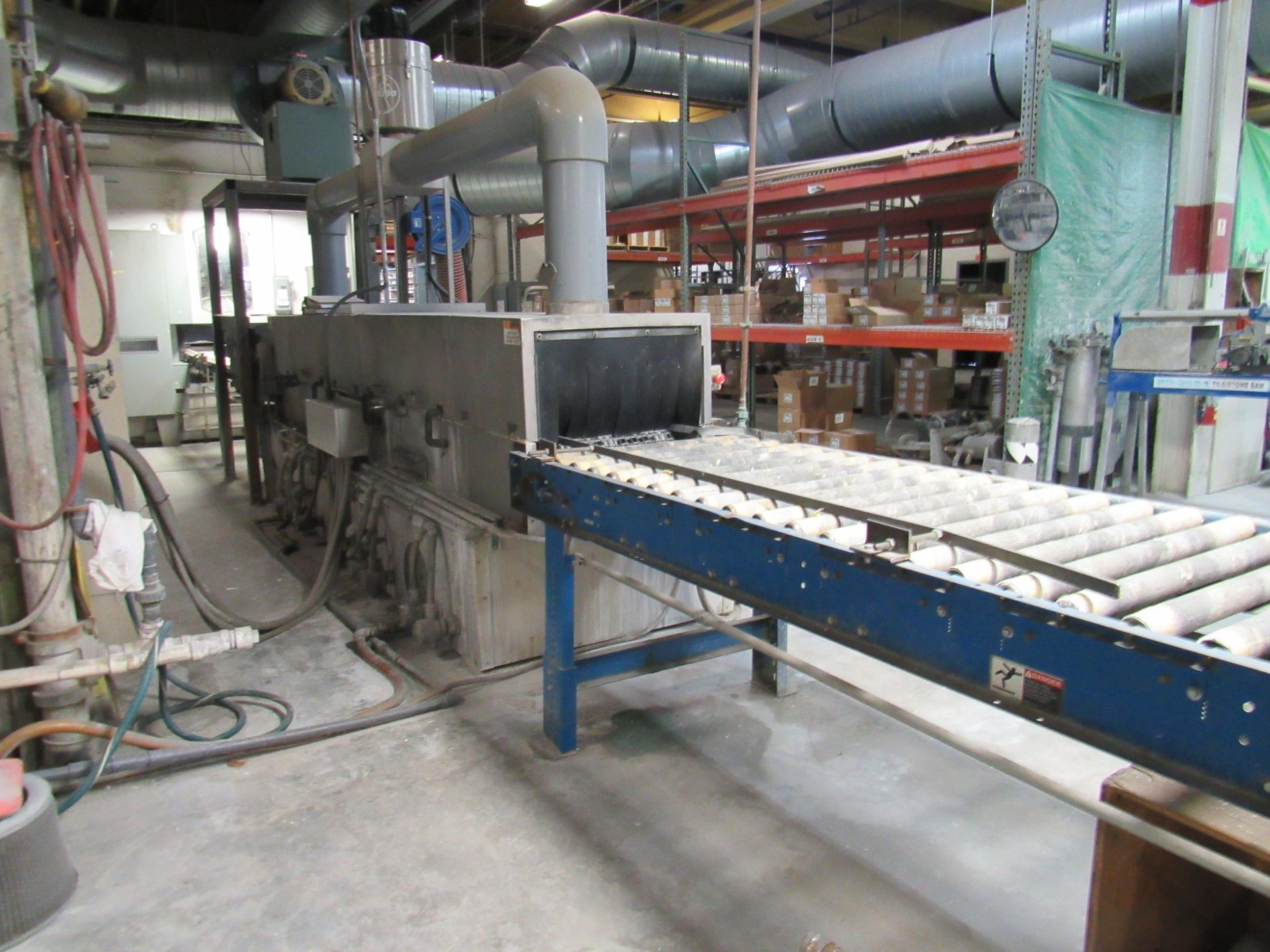 Industrial oven with conveyor belt, pipes, and control panels in a factory setting.