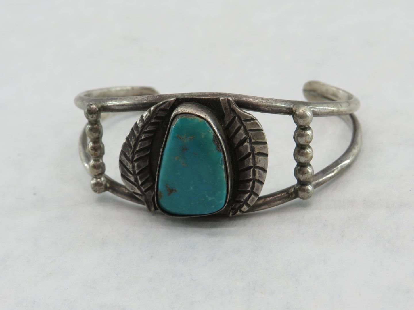 Silver cuff bracelet with turquoise stone, leaf details, and beaded accents.