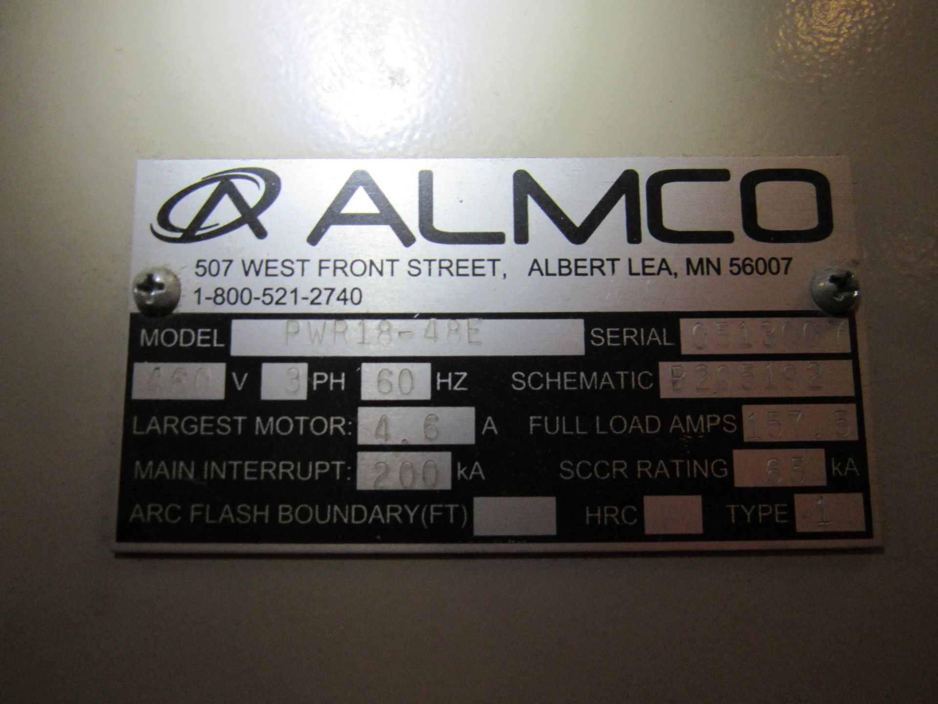 Metal equipment label with the ALMCO logo and text, including model and voltage information.
