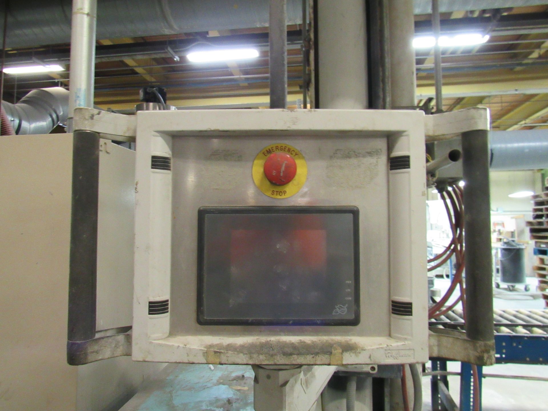 Control panel with red emergency stop button and screen. Mounted on a machine in a factory.