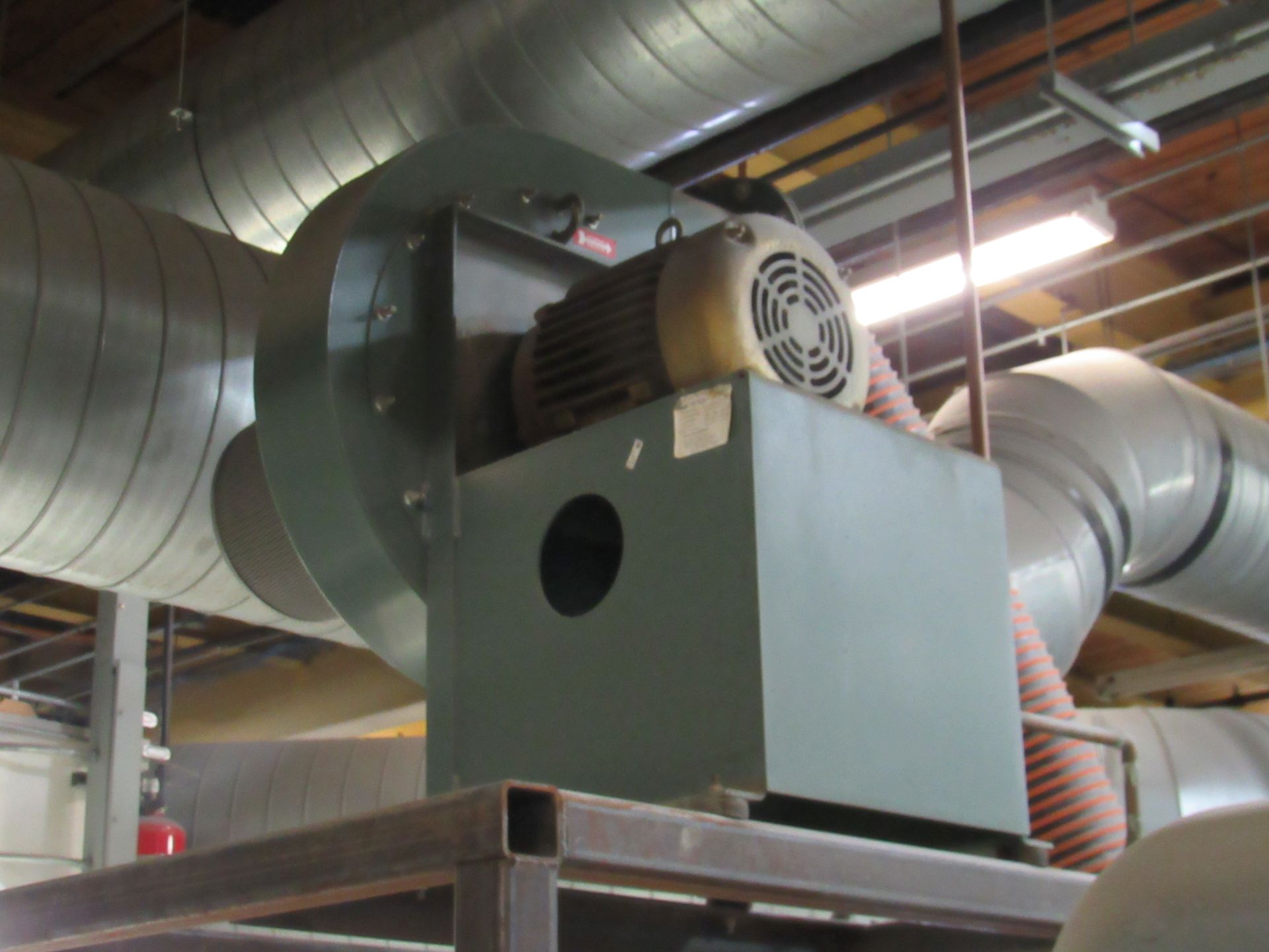 Industrial fan with motor and ductwork, mounted on a metal frame, in a building.