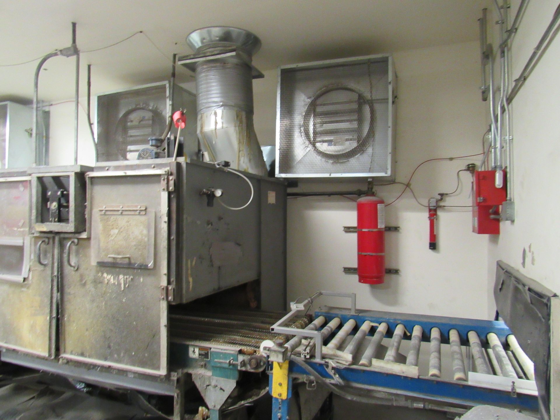 Industrial machinery with ventilation system, metal casing, conveyor belt, and red fire extinguishers.